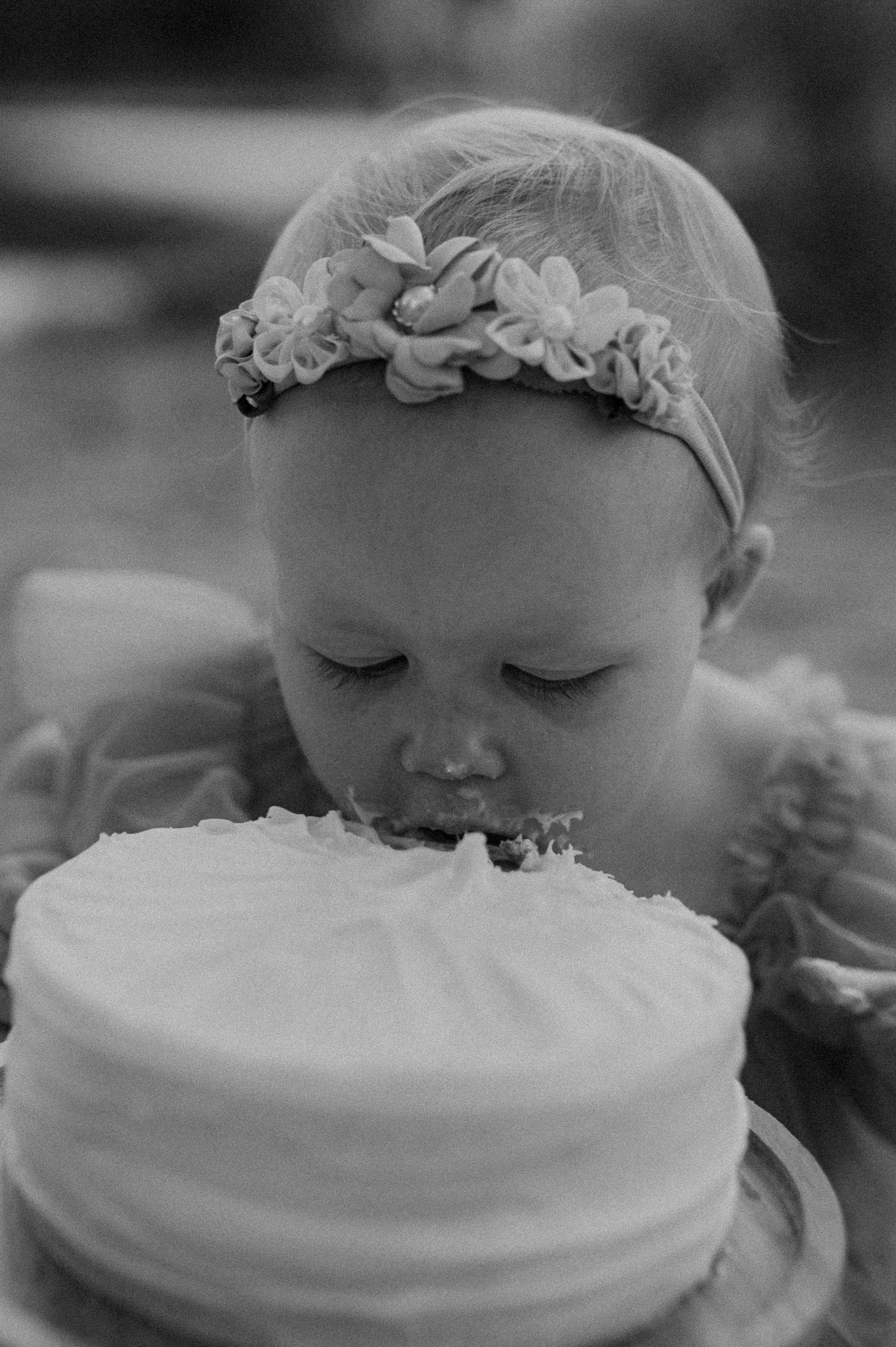 Black and white photo of baby face-planting into white frosted cake.