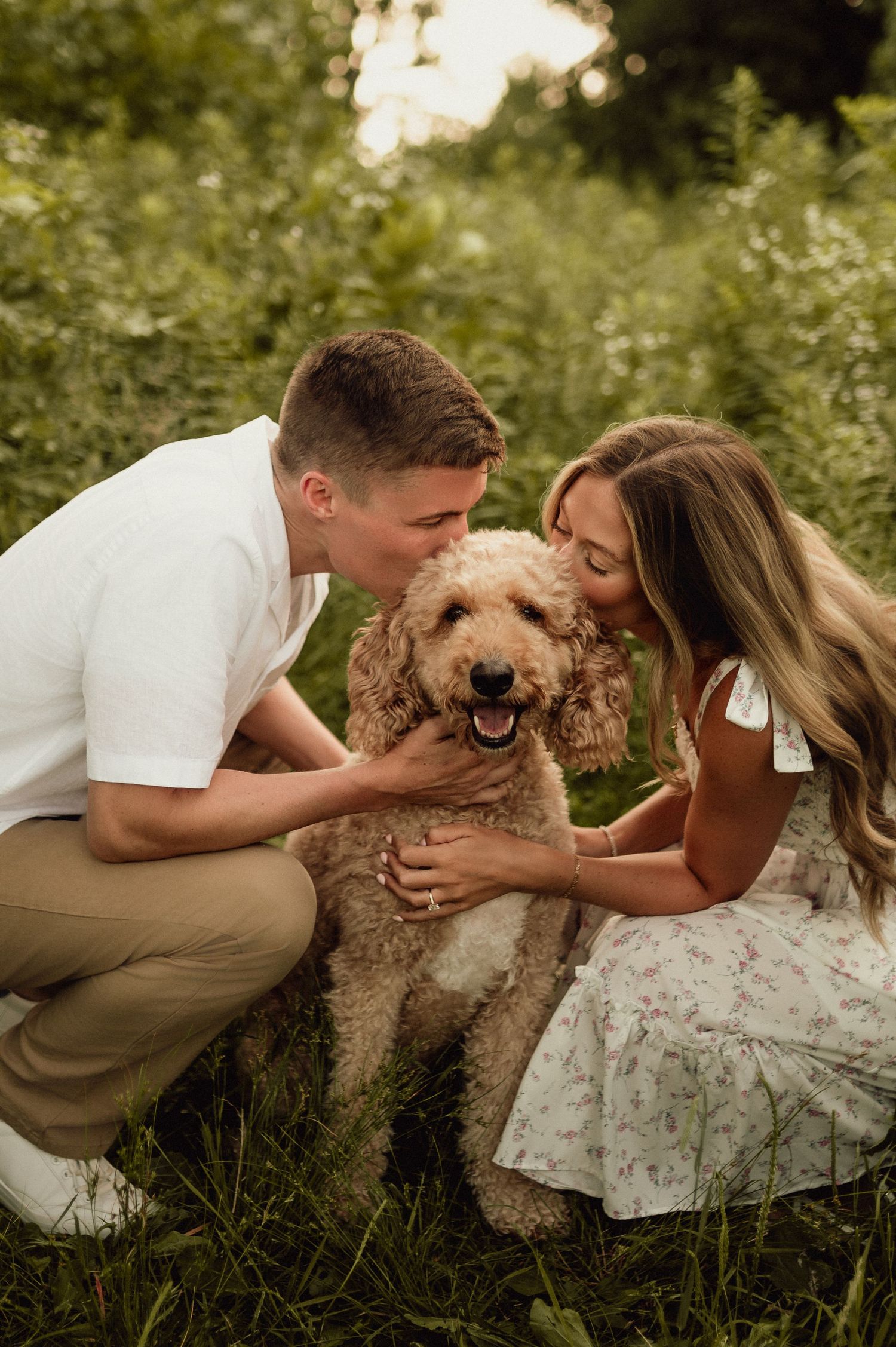 A happy couple plays with their fluffy goldendoodle dog in a grassy outdoor setting.