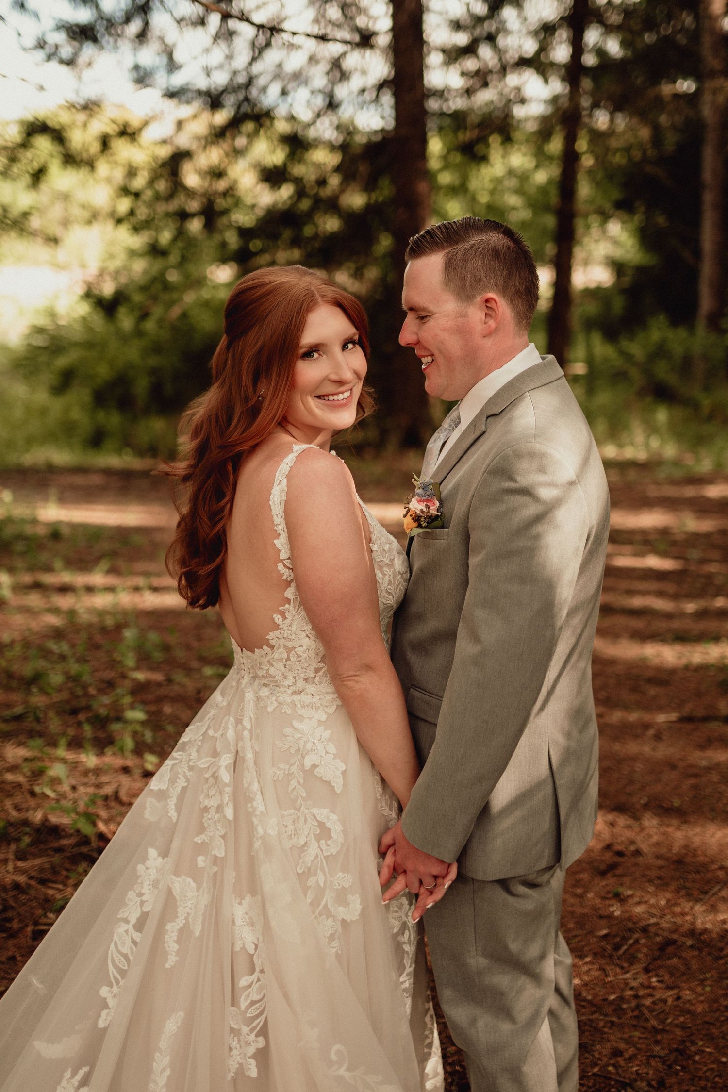 A couple in wedding attire share an intimate moment in a sunlit forest setting with fallen autumn leaves.