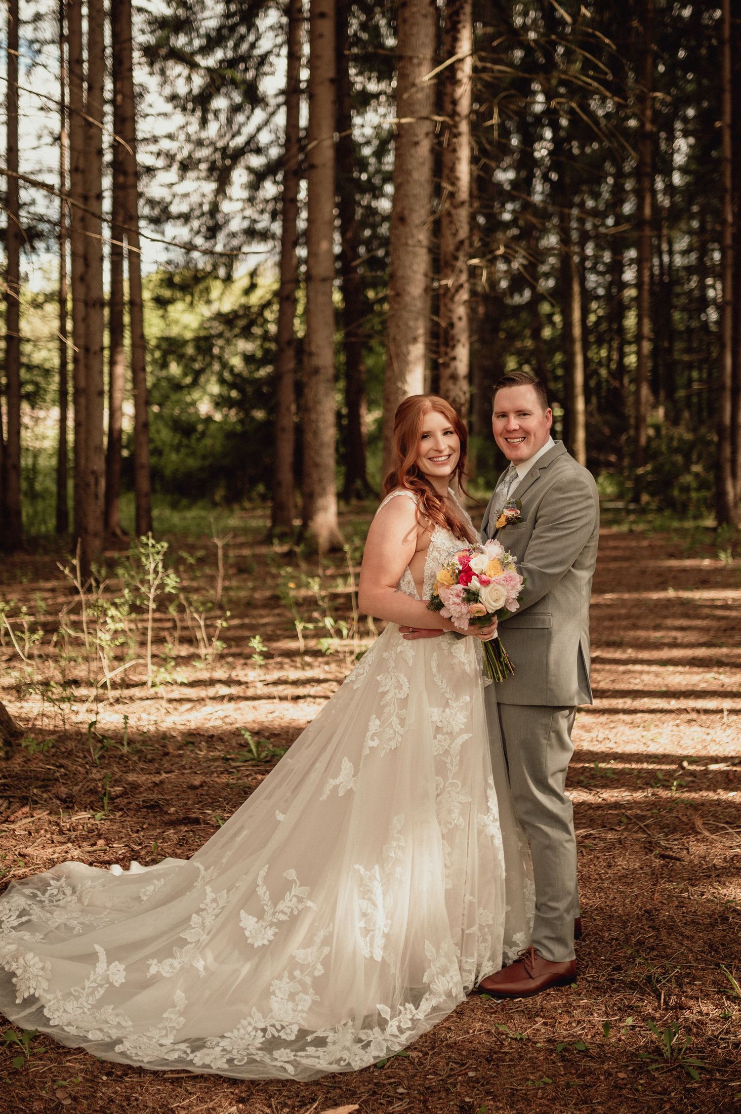 A couple shares a romantic moment in a sunlit forest setting during their wedding photoshoot.