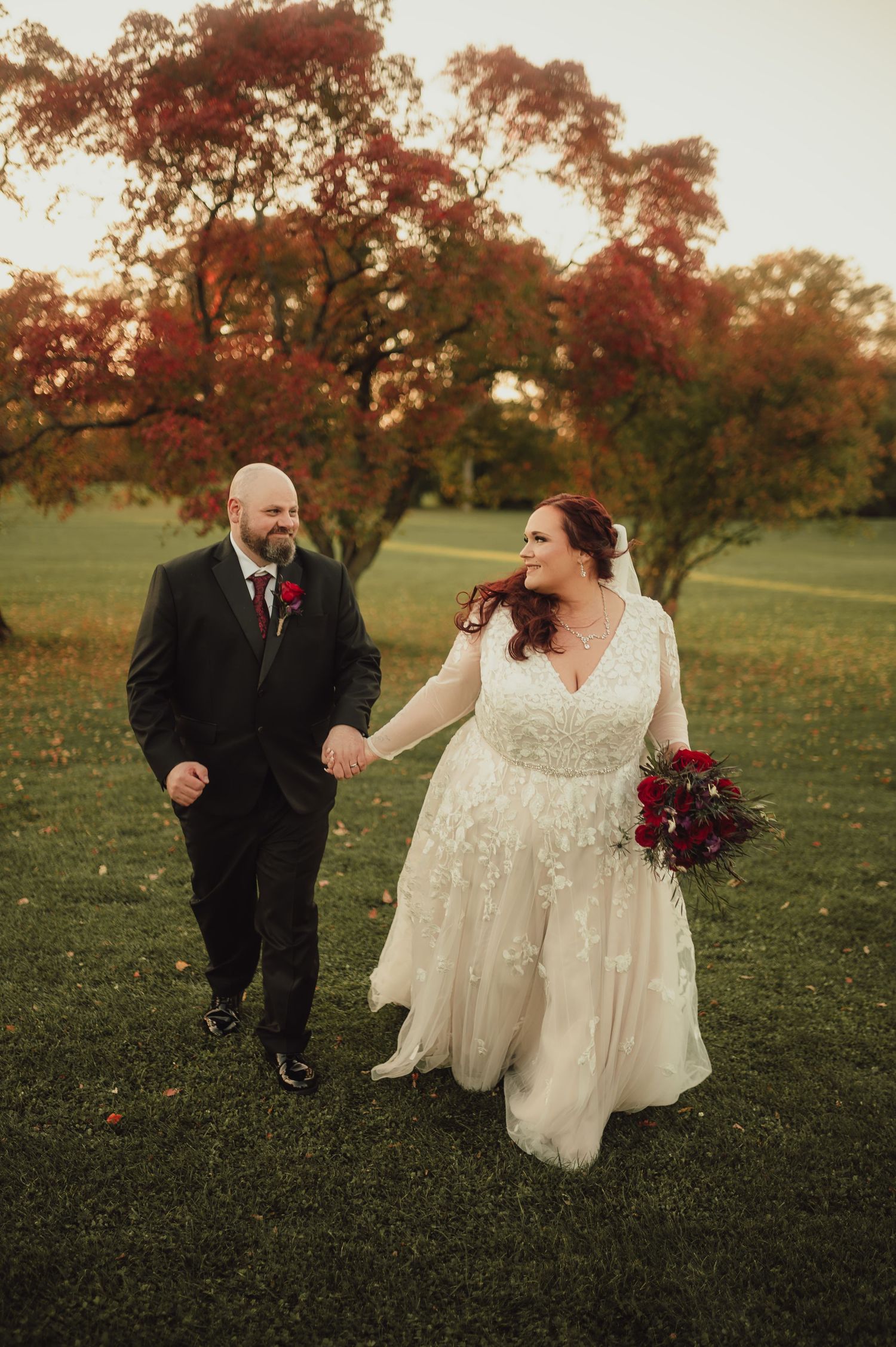 A couple walking together on grass during autumn with fall foliage in the background.