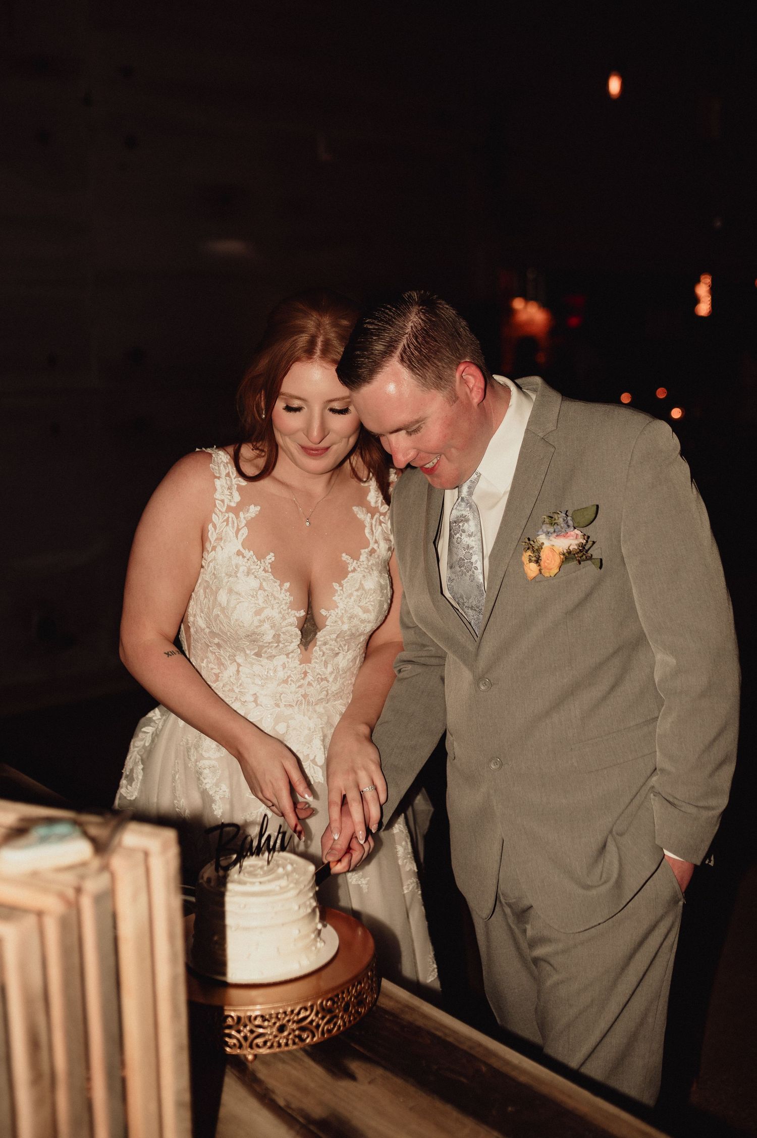A couple in wedding attire cuts their white wedding cake together during an evening reception celebration.