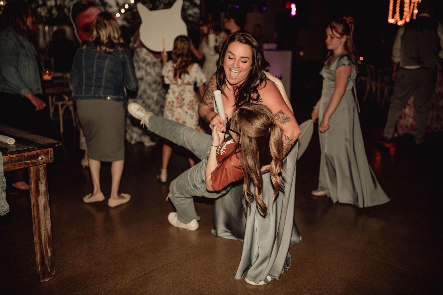 Couples dancing together at a dimly lit social event with other attendees visible in the background.
