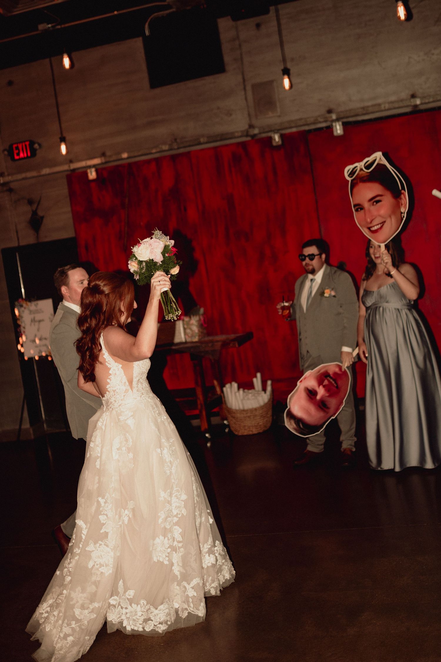 Wedding couple dances together on dark dance floor with string lights overhead and red curtain backdrop.