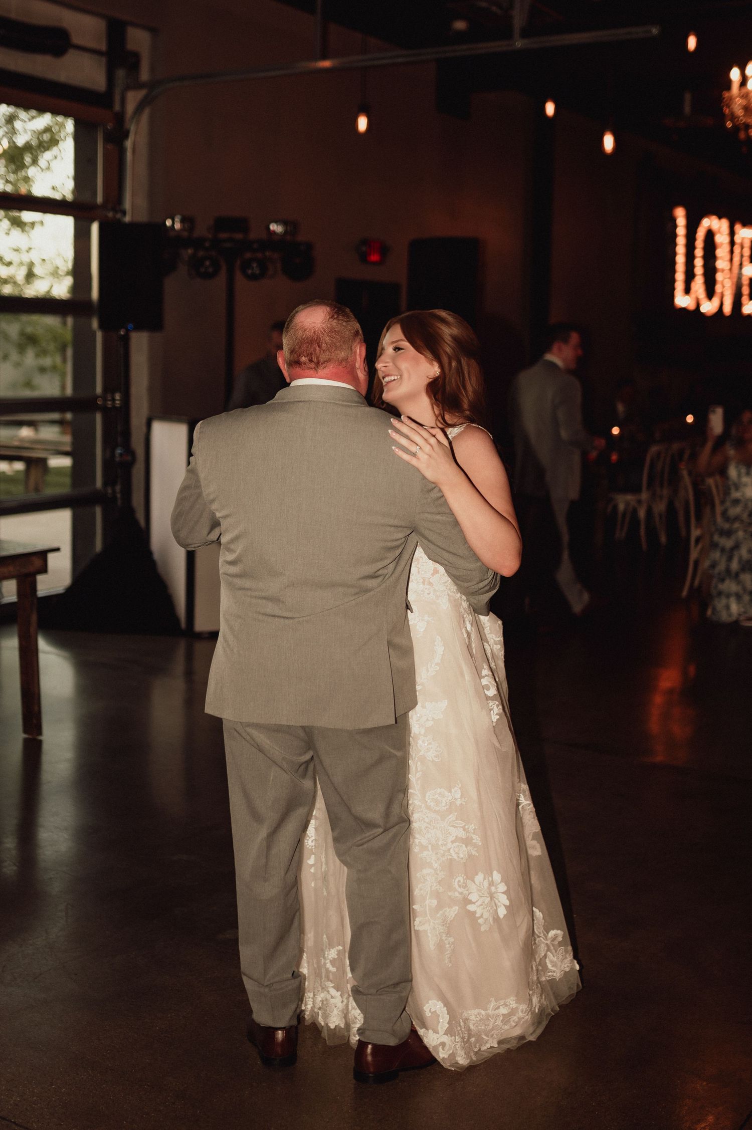 A couple in wedding attire shares a romantic dance together in a dimly lit reception venue.