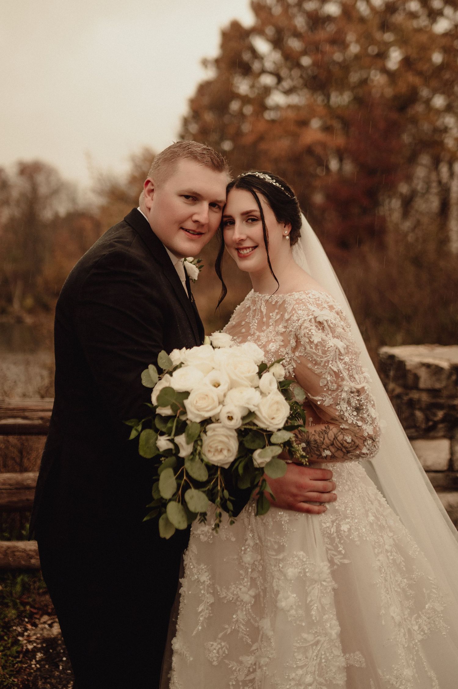 A romantic wedding couple embraces in an autumn setting with white roses and lace details.