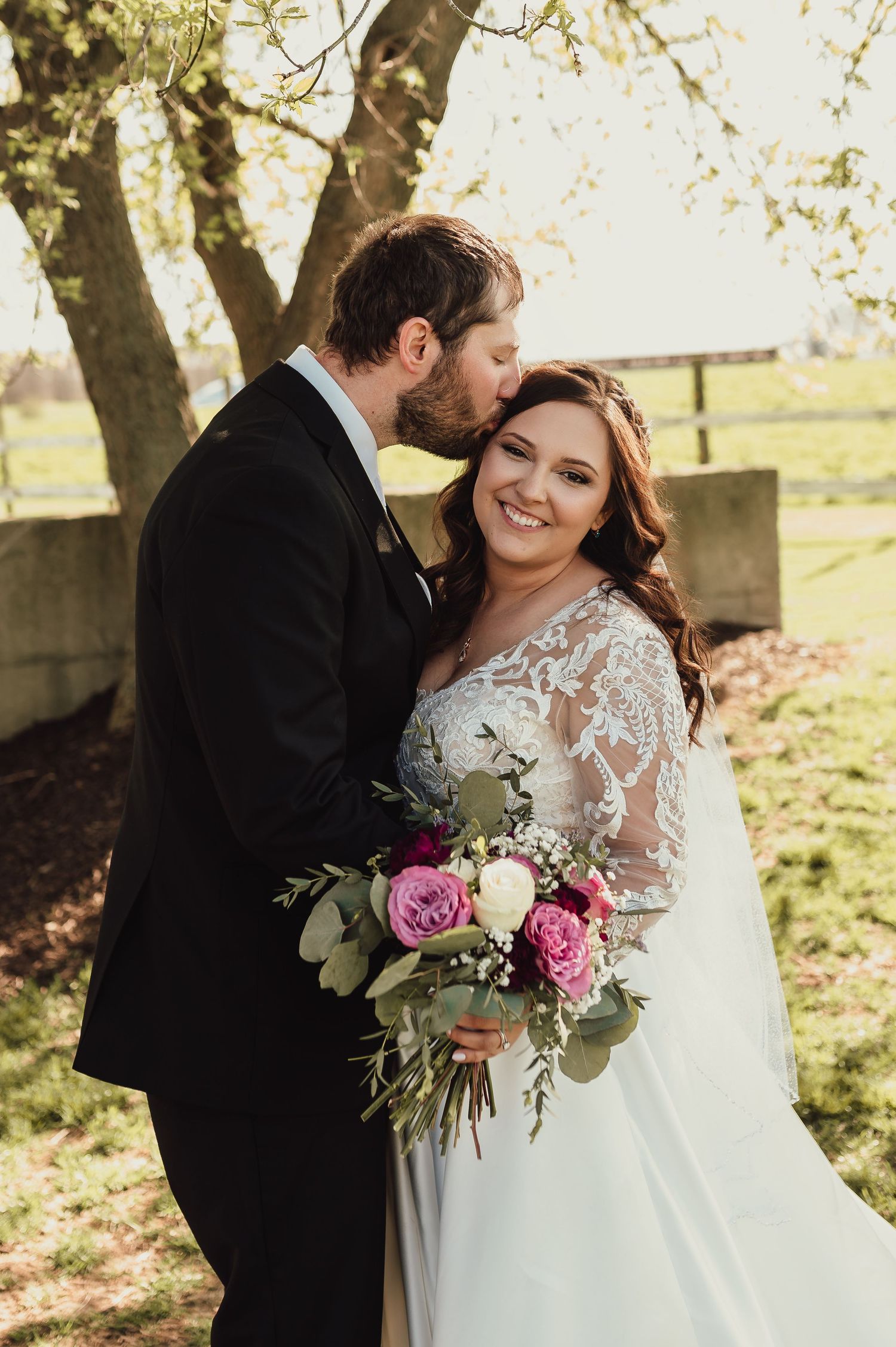 Wedding couple sharing intimate moment with pink floral bouquet in outdoor setting.