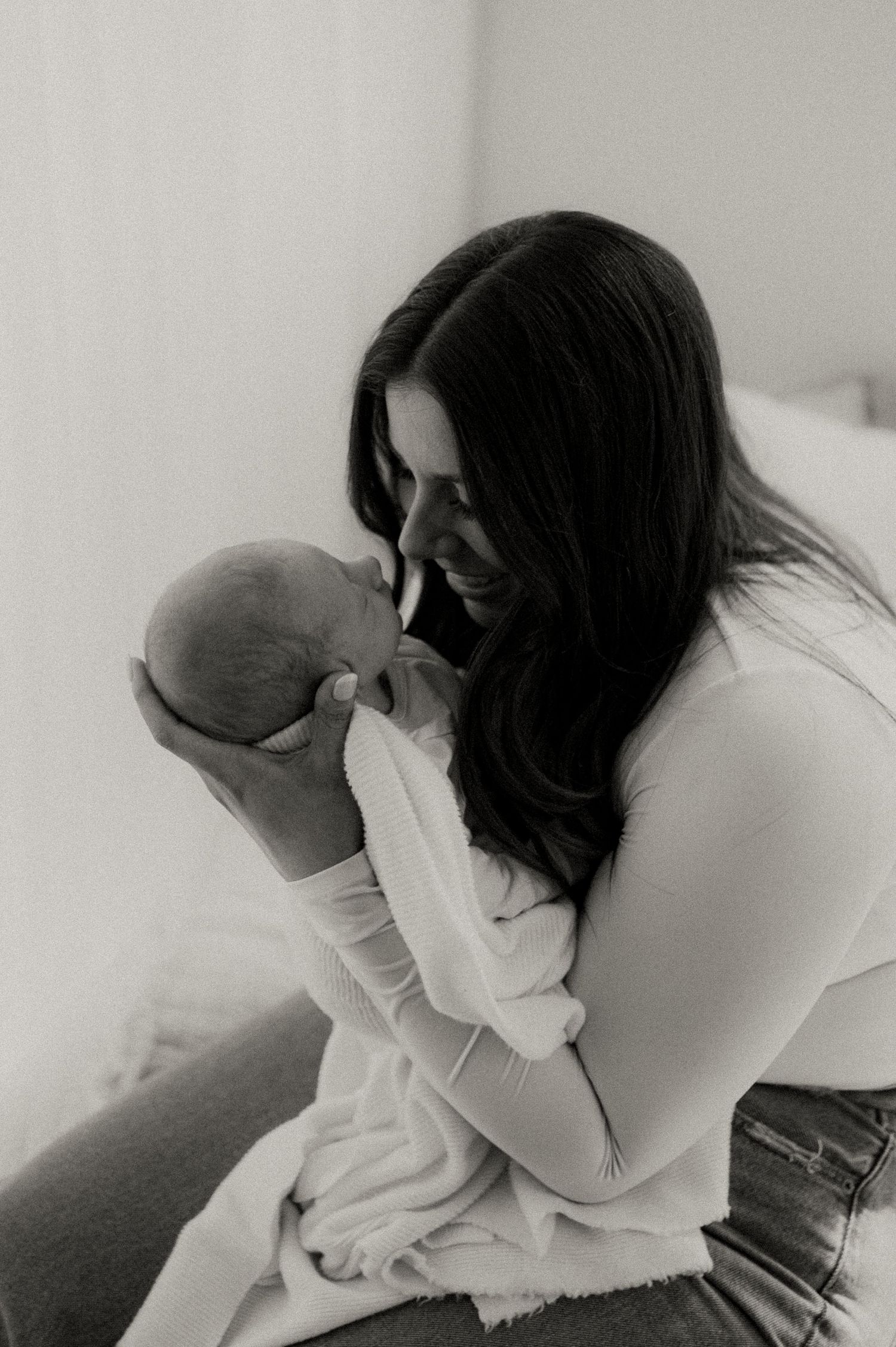 Mother in white sweater tenderly holding and kissing newborn baby.