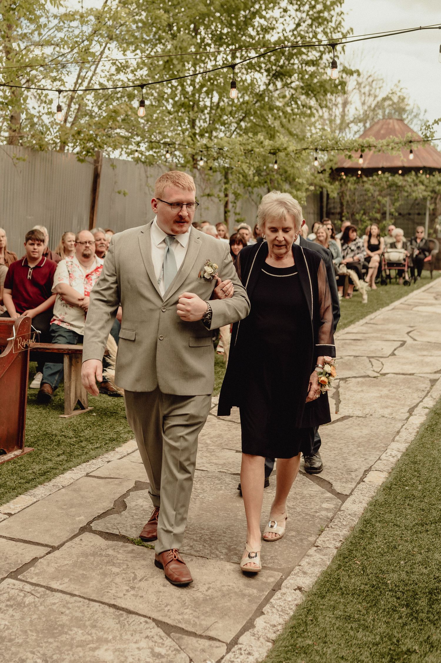 A couple dancing together at an outdoor event, with the man wearing a gray suit and woman in black dress.