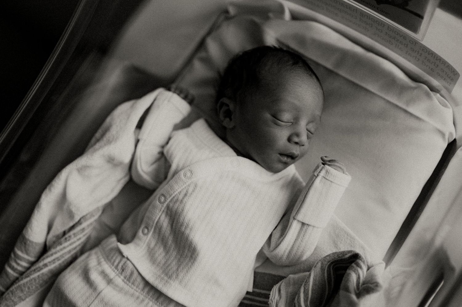Sleeping newborn baby in white clothing resting in hospital bed.