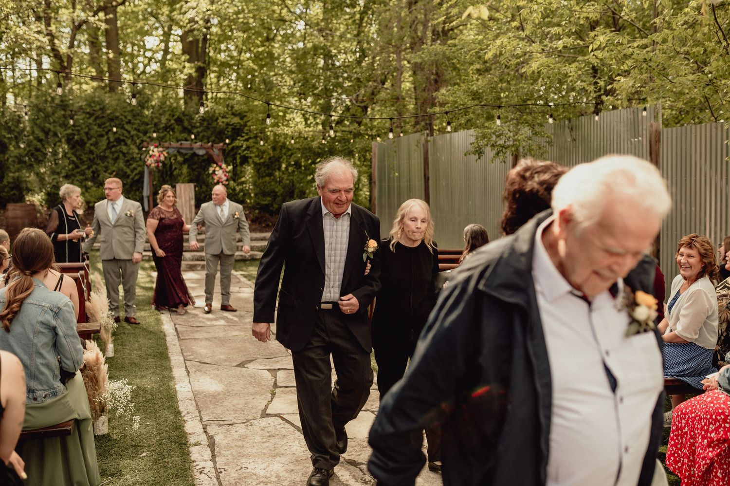 A large group of wedding guests gathered outdoors in a wooded area during a celebration.