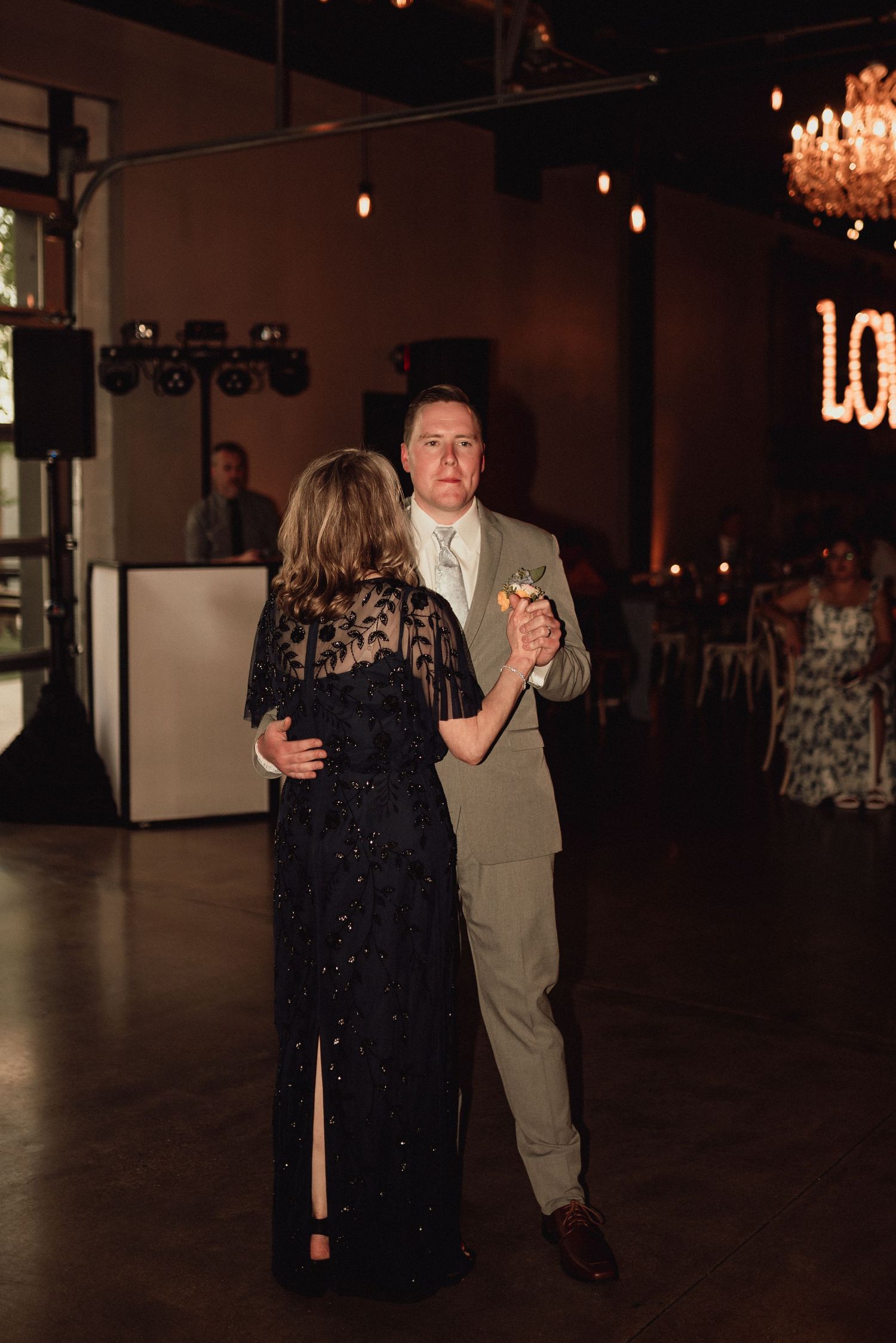 A couple dances together in a dimly lit venue with string lights and chandeliers overhead.