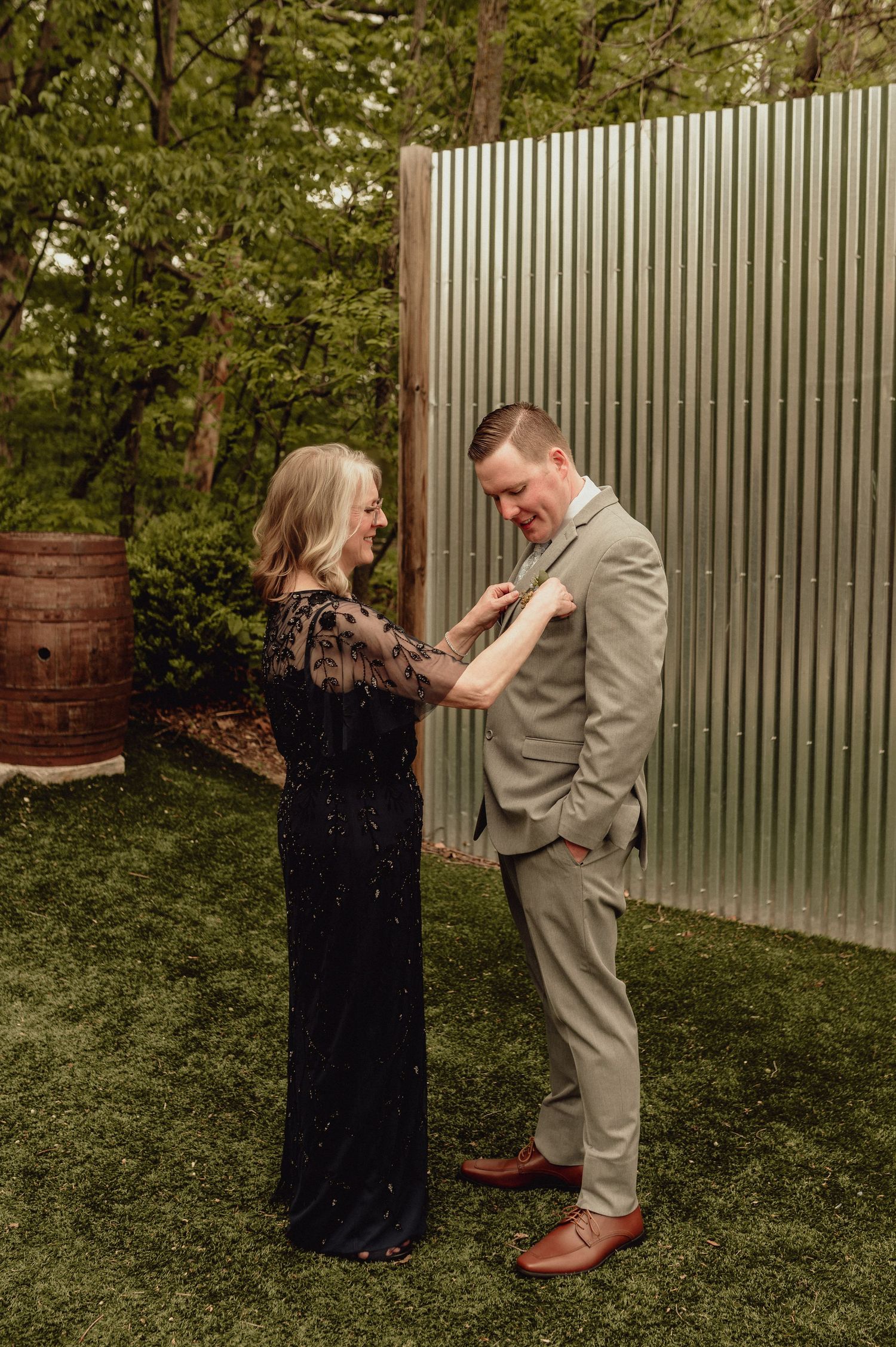 A couple shares a joyful moment together in a garden setting with a corrugated metal fence backdrop.