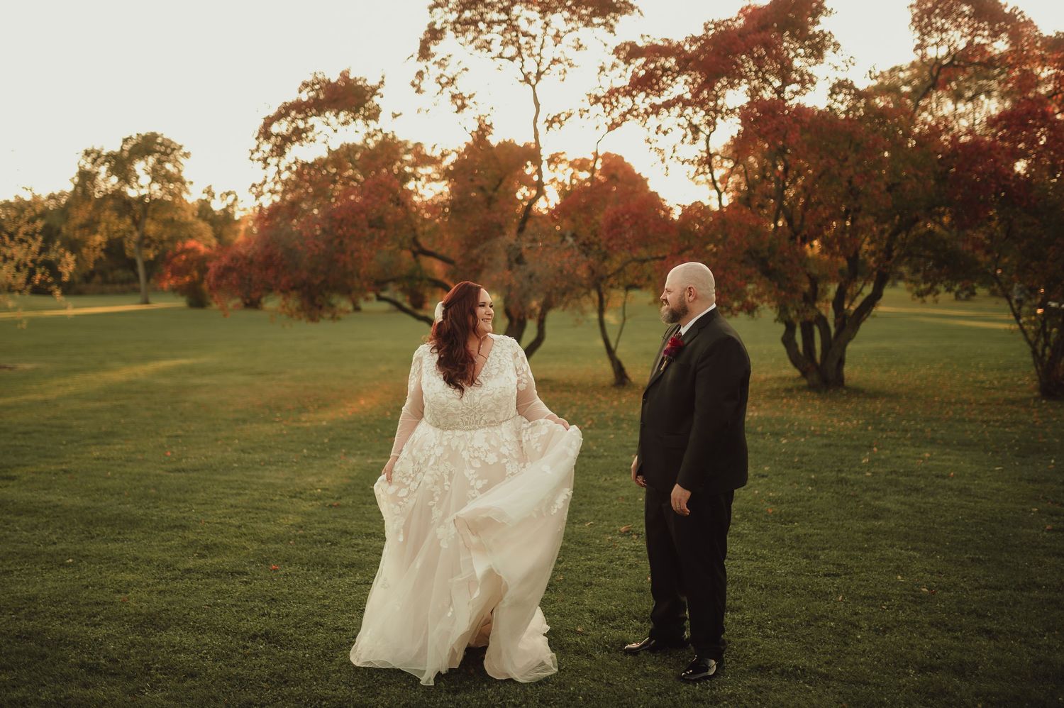 A romantic wedding portrait in a scenic field with autumn trees.