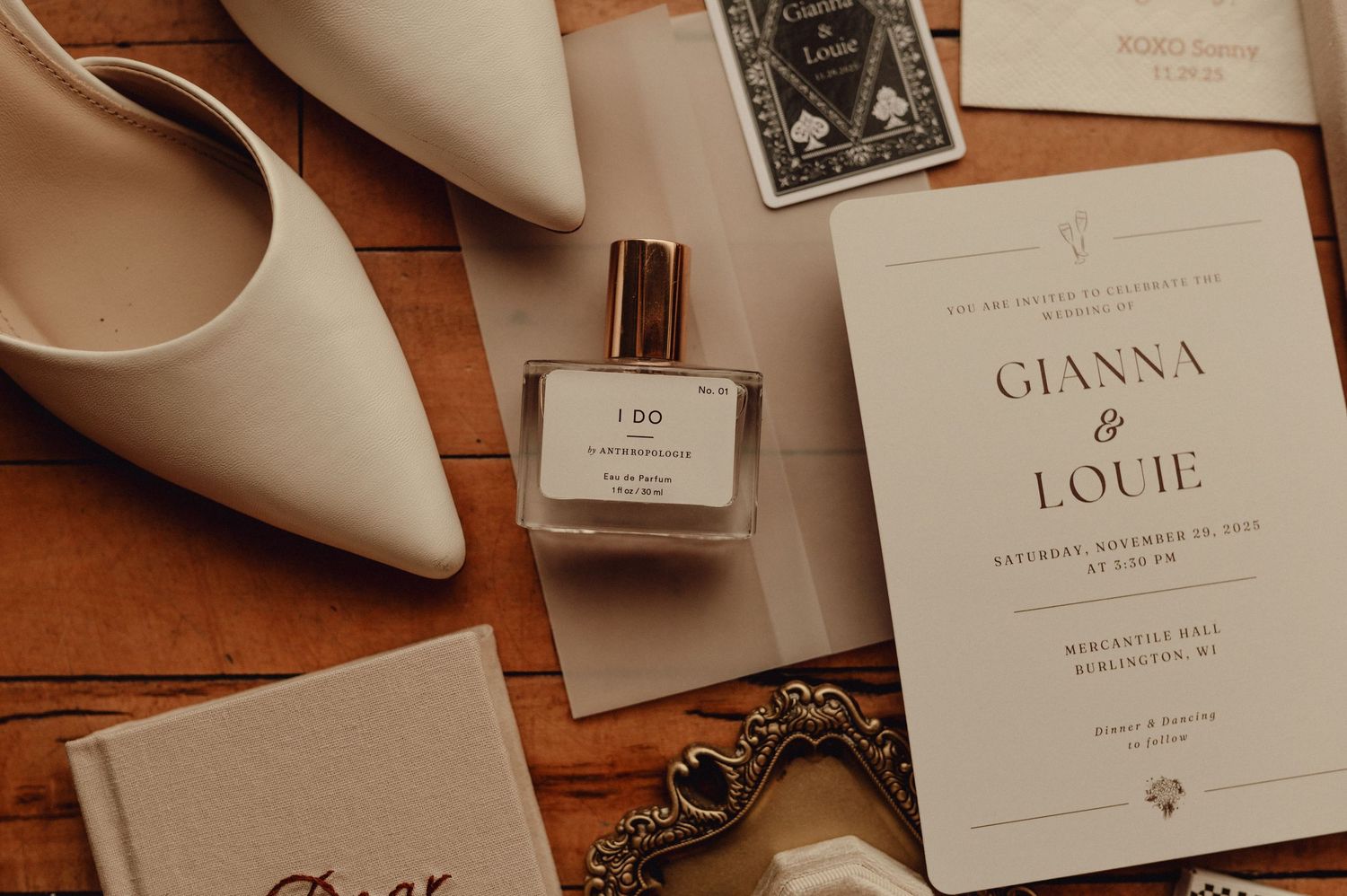 Wedding invitation details and place cards arranged on wooden surface with white heels in elegant composition.