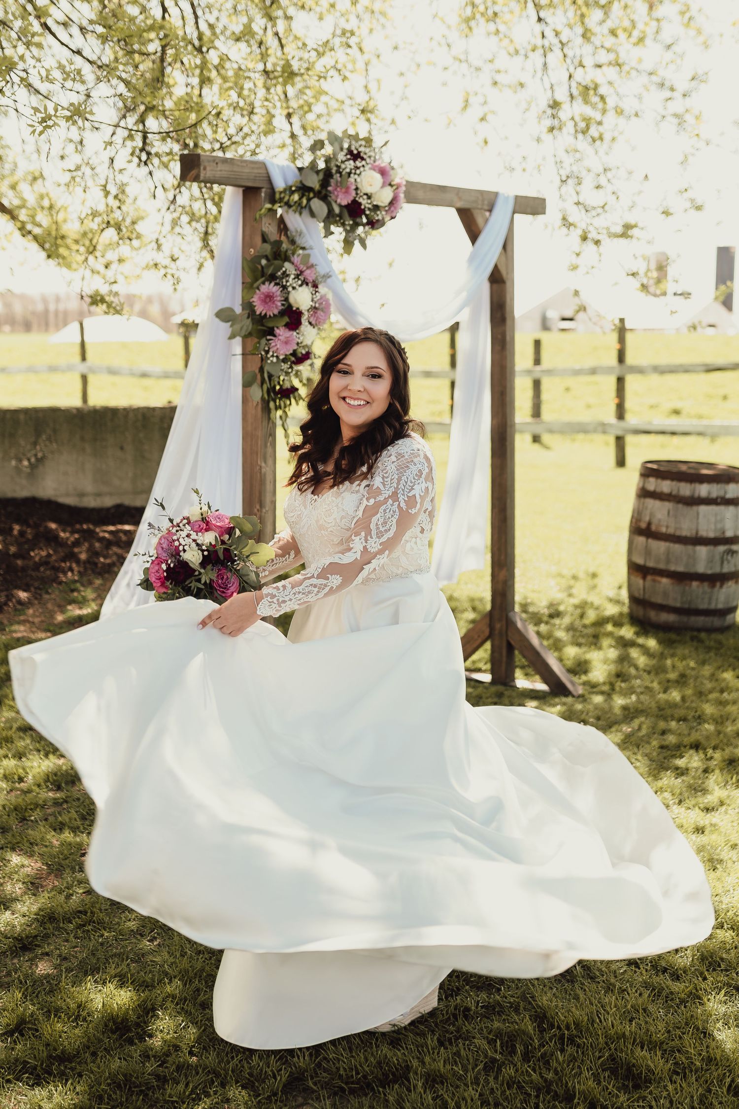 Bride twirling in white lace wedding dress outdoors in sunlit garden setting.