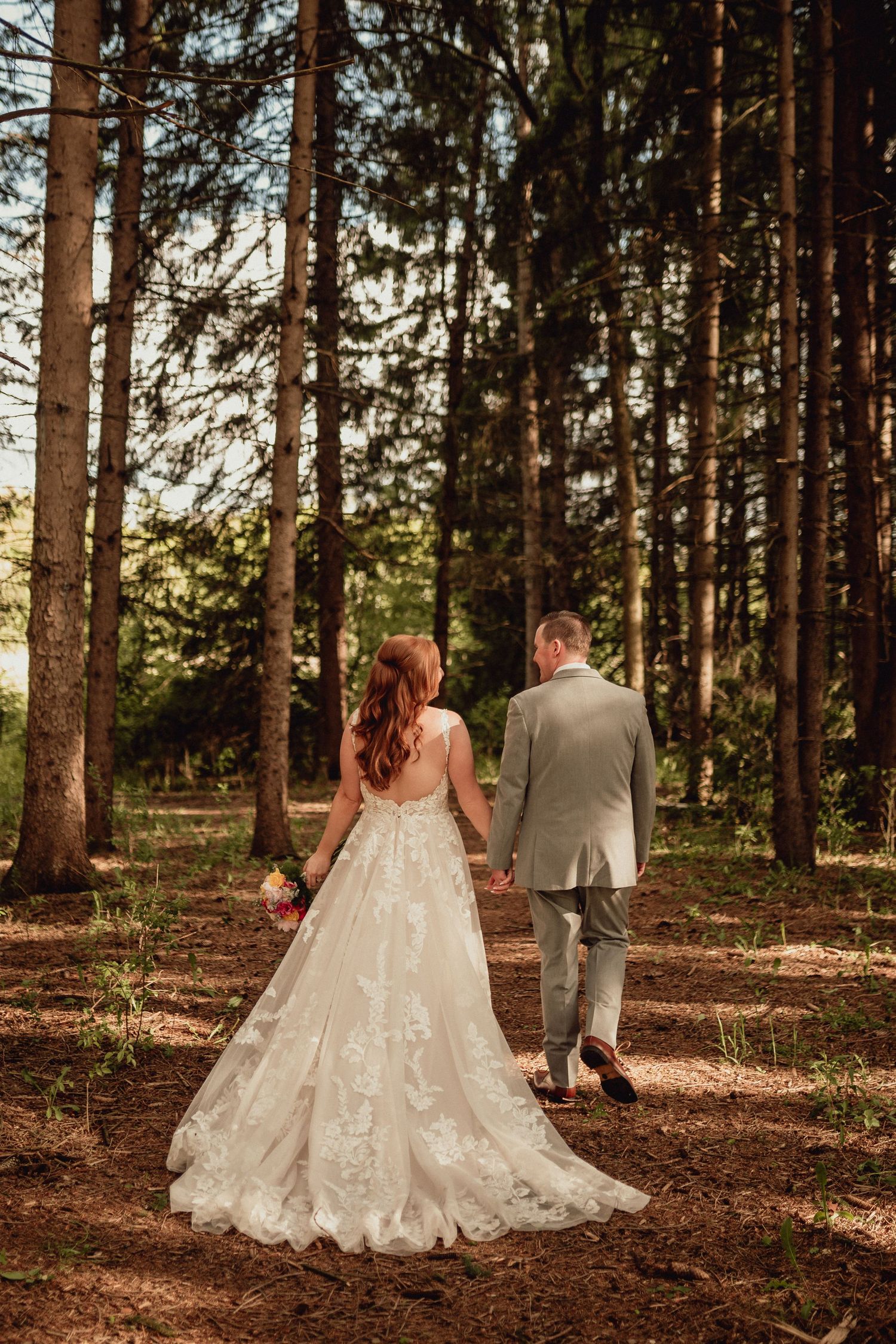 A couple in wedding attire walks through a serene pine forest during golden hour, creating a romantic woodland scene.