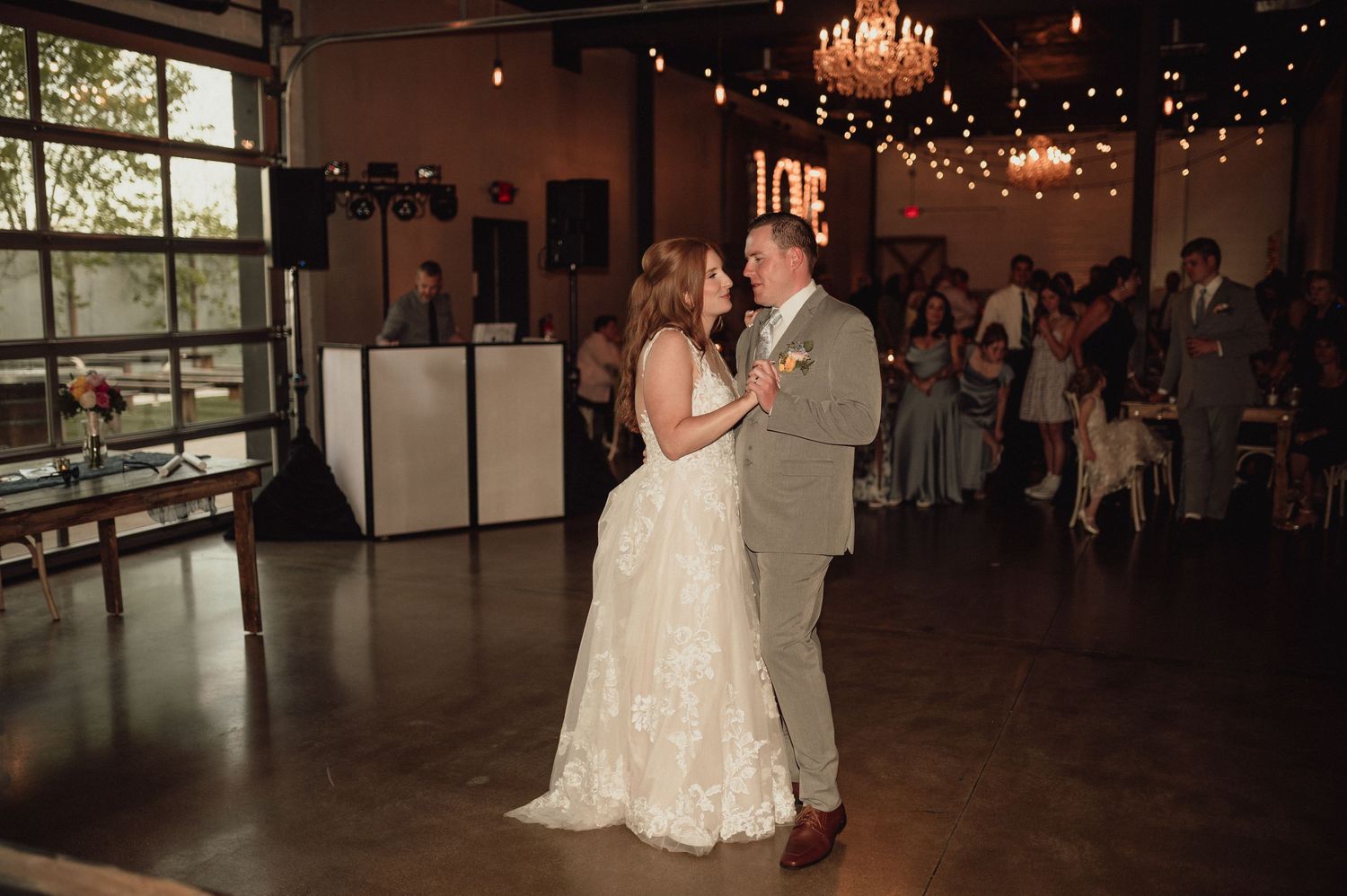 A couple shares their first dance at a romantic wedding reception under twinkling lights and chandeliers.