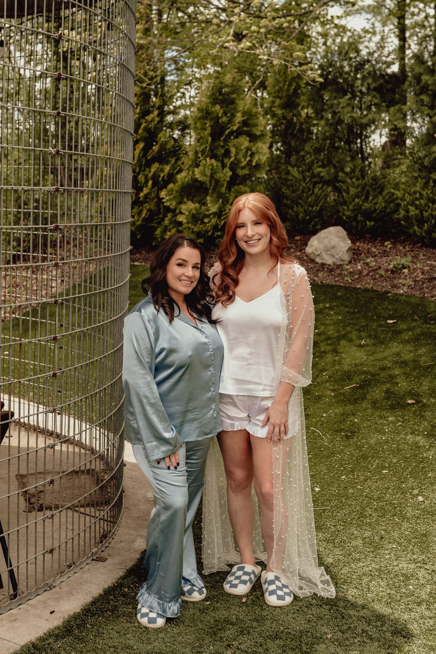 Two people pose together outdoors wearing matching white platform sandals in a garden setting.