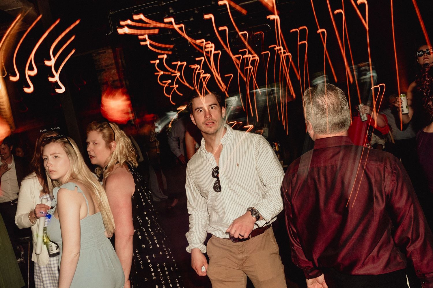 People dancing and socializing at a dimly lit party or nightclub with red lighting effects.