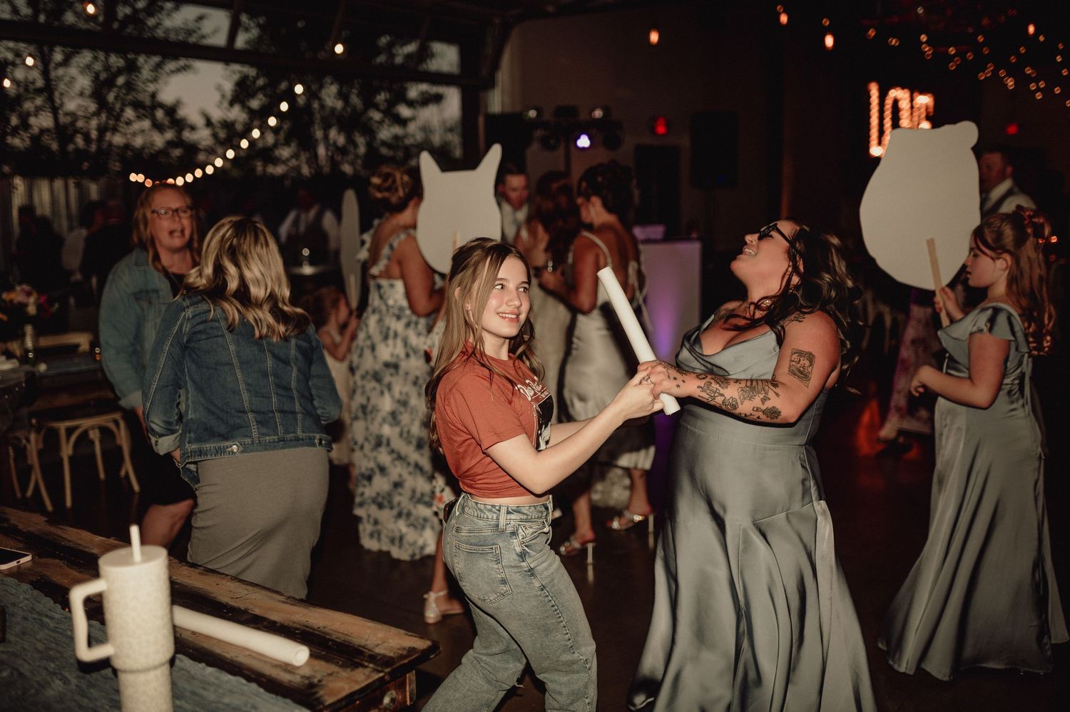 People dancing and socializing at a dimly lit party venue with string lights overhead.