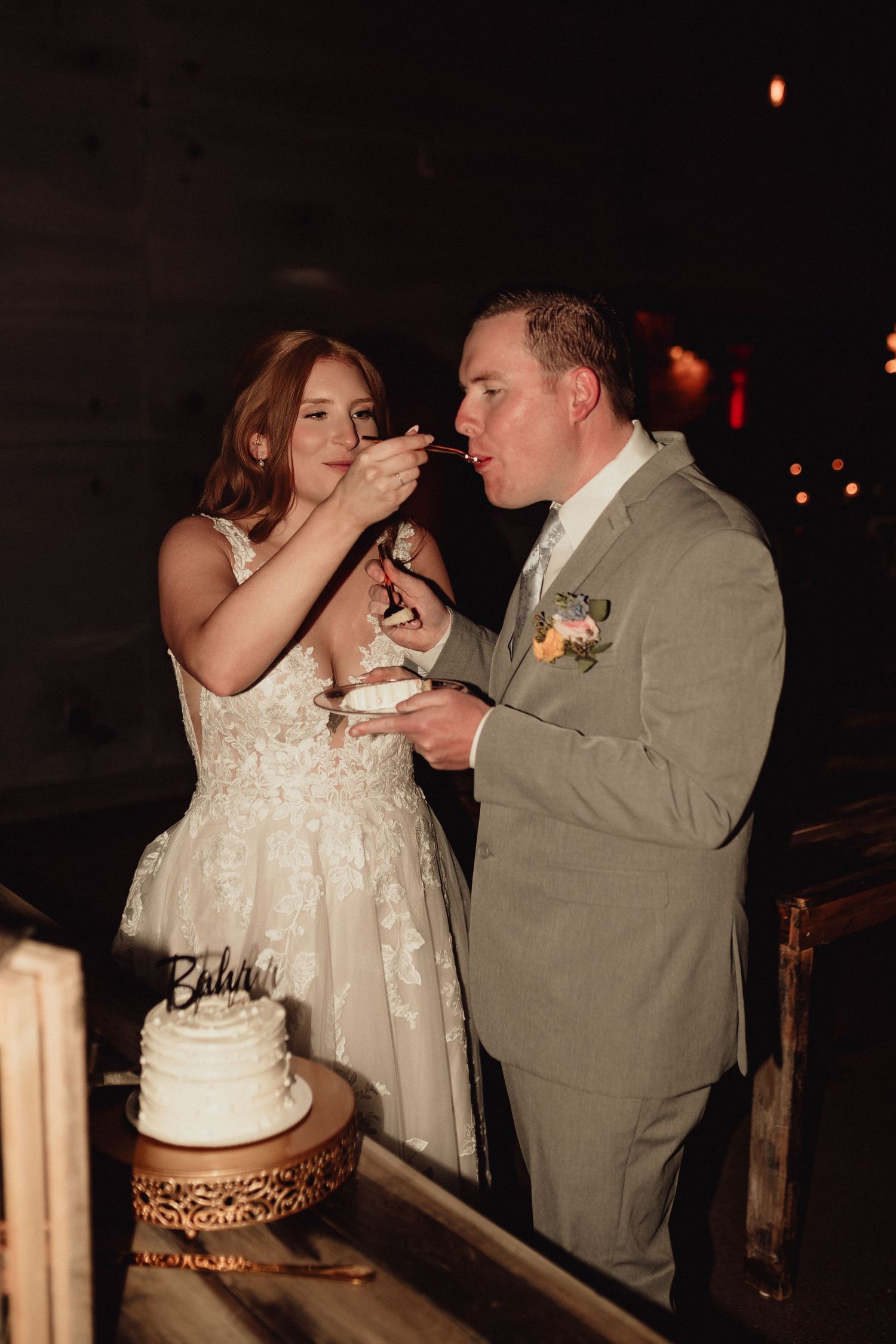 Newlyweds share their first bite of wedding cake together in a romantic candlelit reception setting.