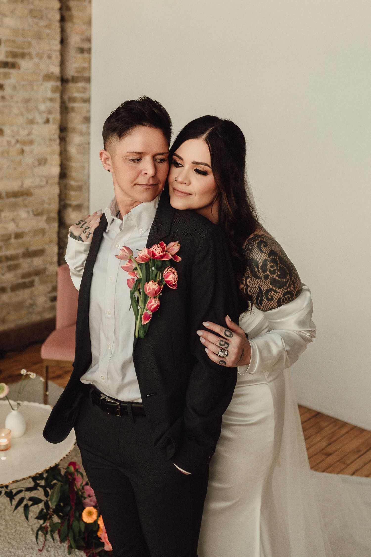 Romantic couple embraces in minimalist indoor setting with coral floral accents.