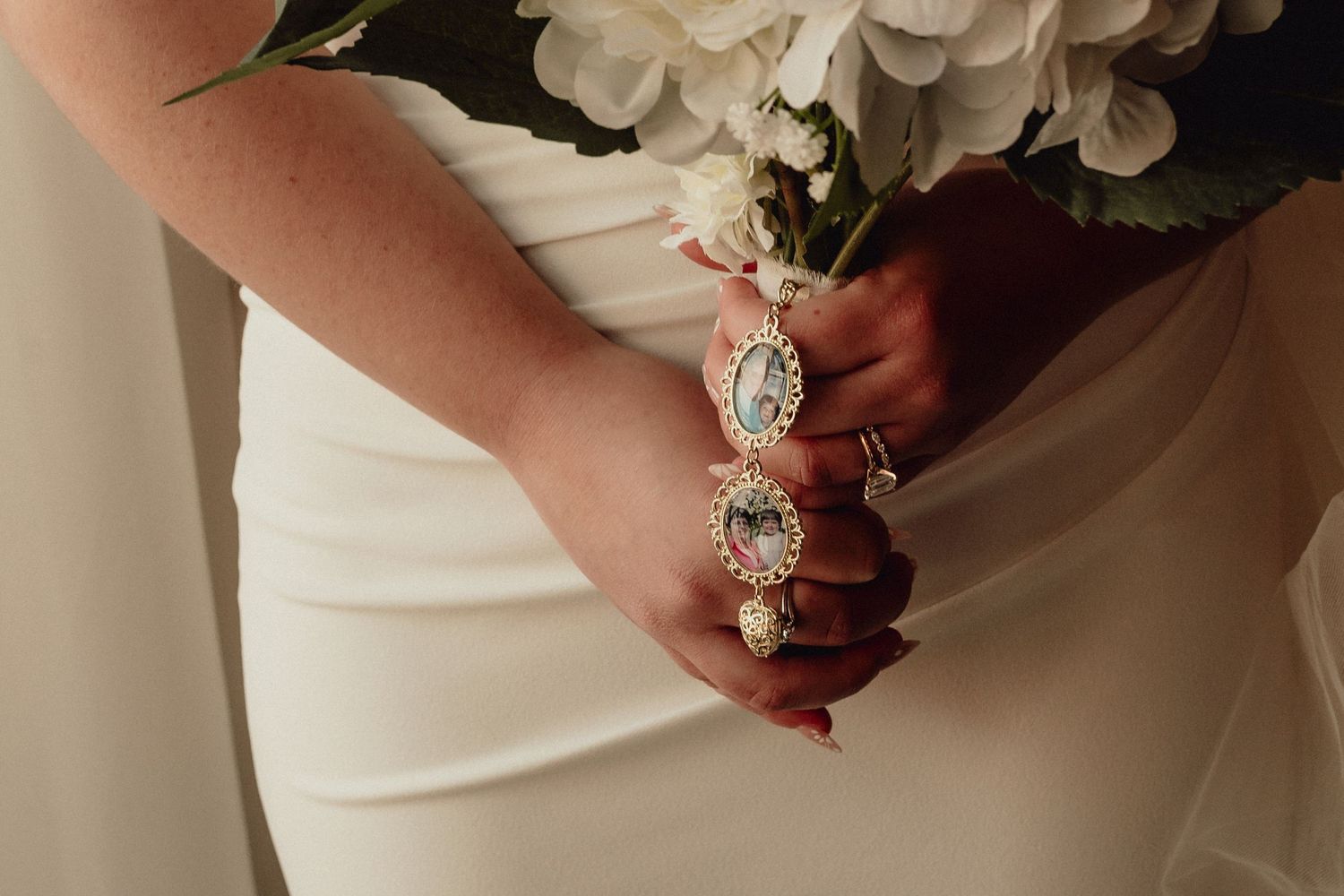 Close-up of hands holding a bridal bouquet with red and white flowers against a white wedding dress.