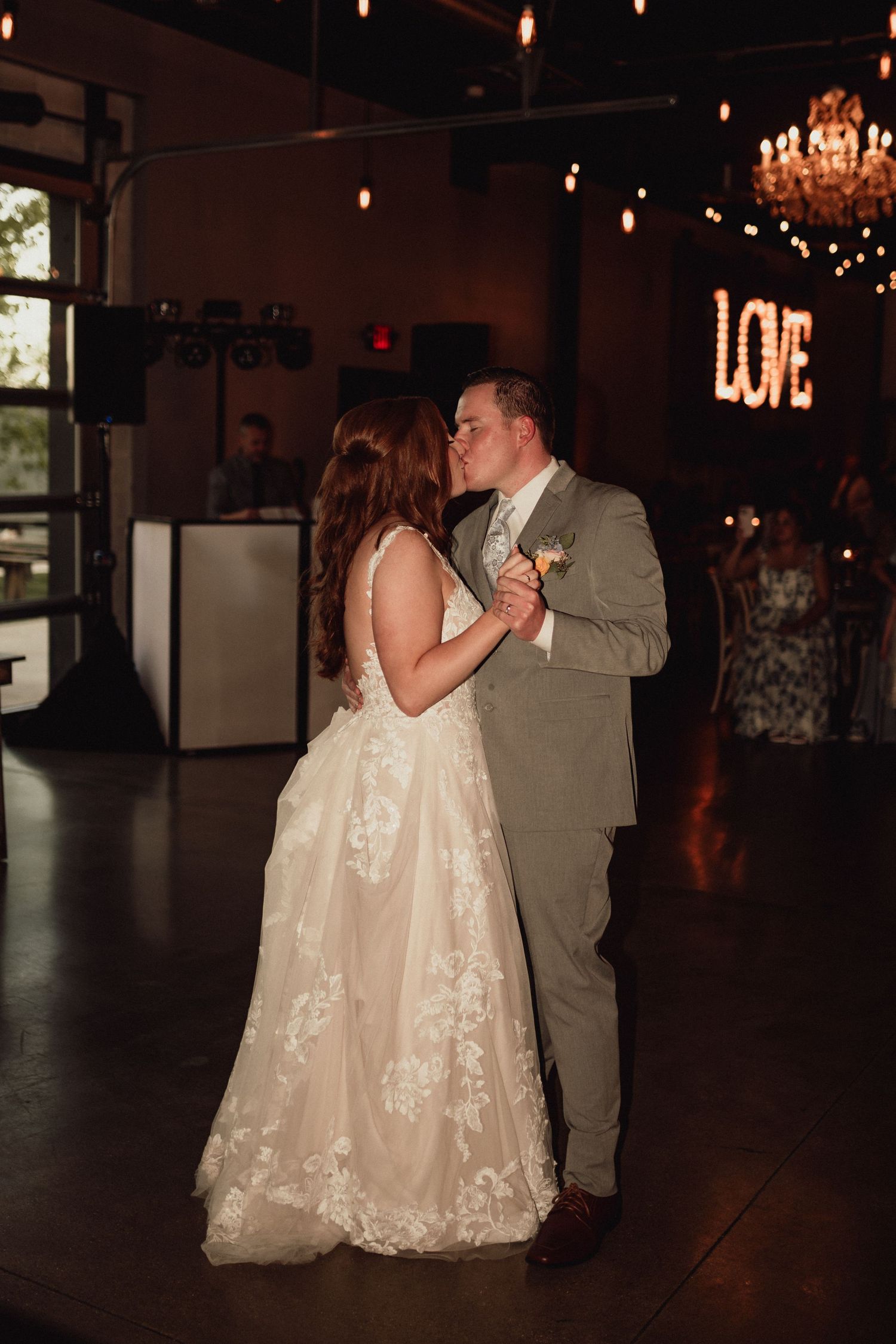 A couple shares their first dance at a wedding reception with a glowing LOVE sign illuminated in the background.