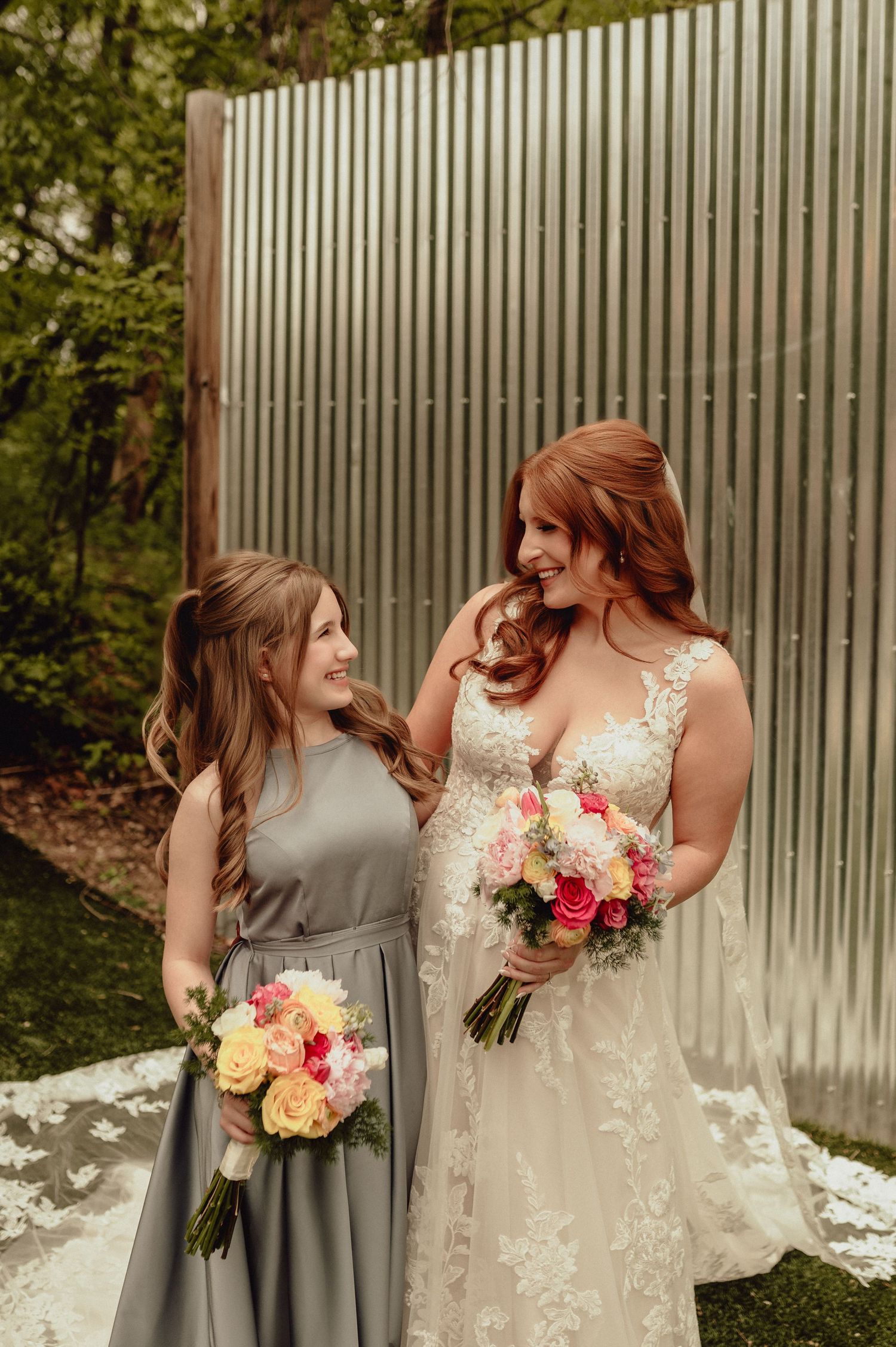 Two people in wedding attire share a candid laughing moment together against a corrugated metal wall backdrop.