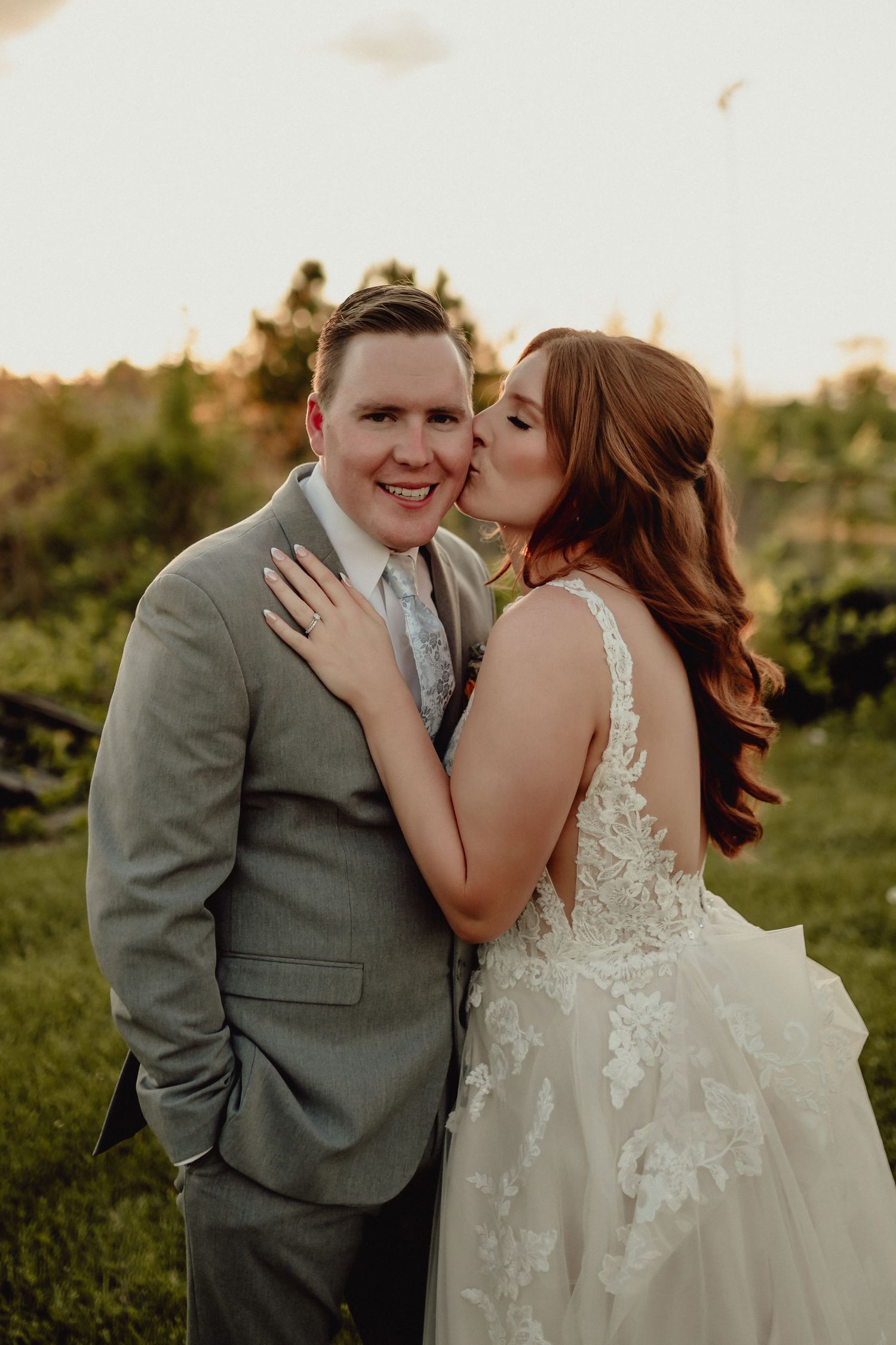 A romantic wedding couple embraces in a sunlit field during golden hour.