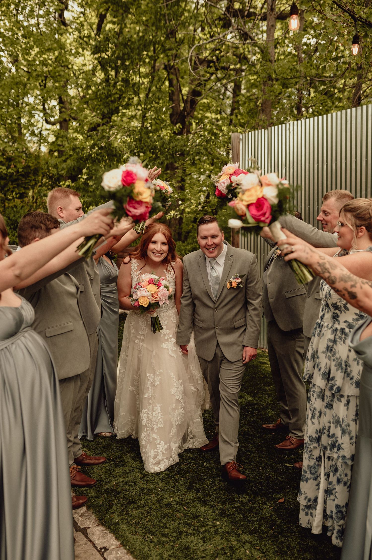 Wedding party in gray attire strikes playful dabbing poses in an outdoor garden setting.