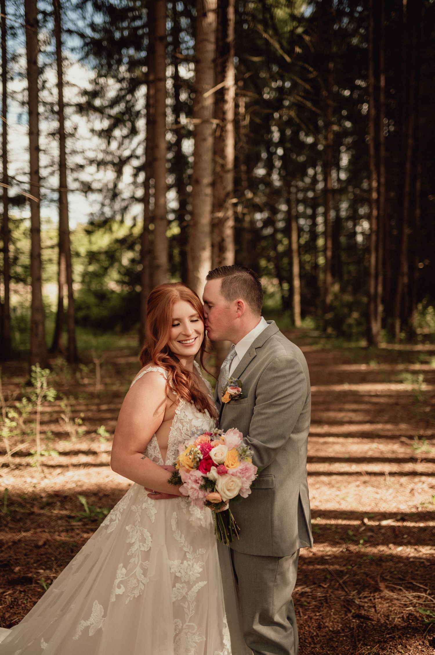A romantic wedding couple shares intimate moments in a sunlit forest setting with pine trees and autumn leaves.