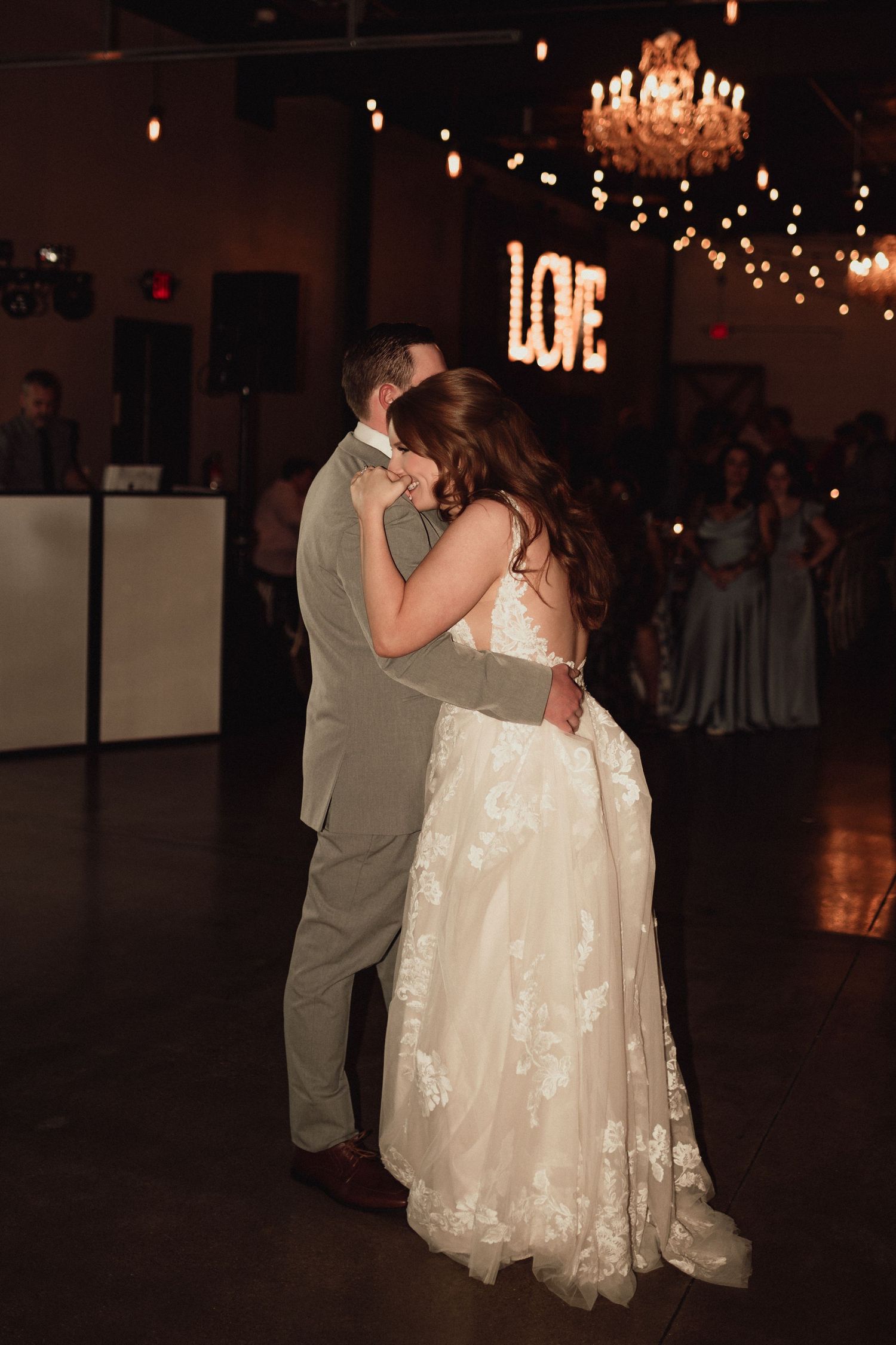 A couple shares their first dance as newlyweds under soft lighting at their wedding reception.