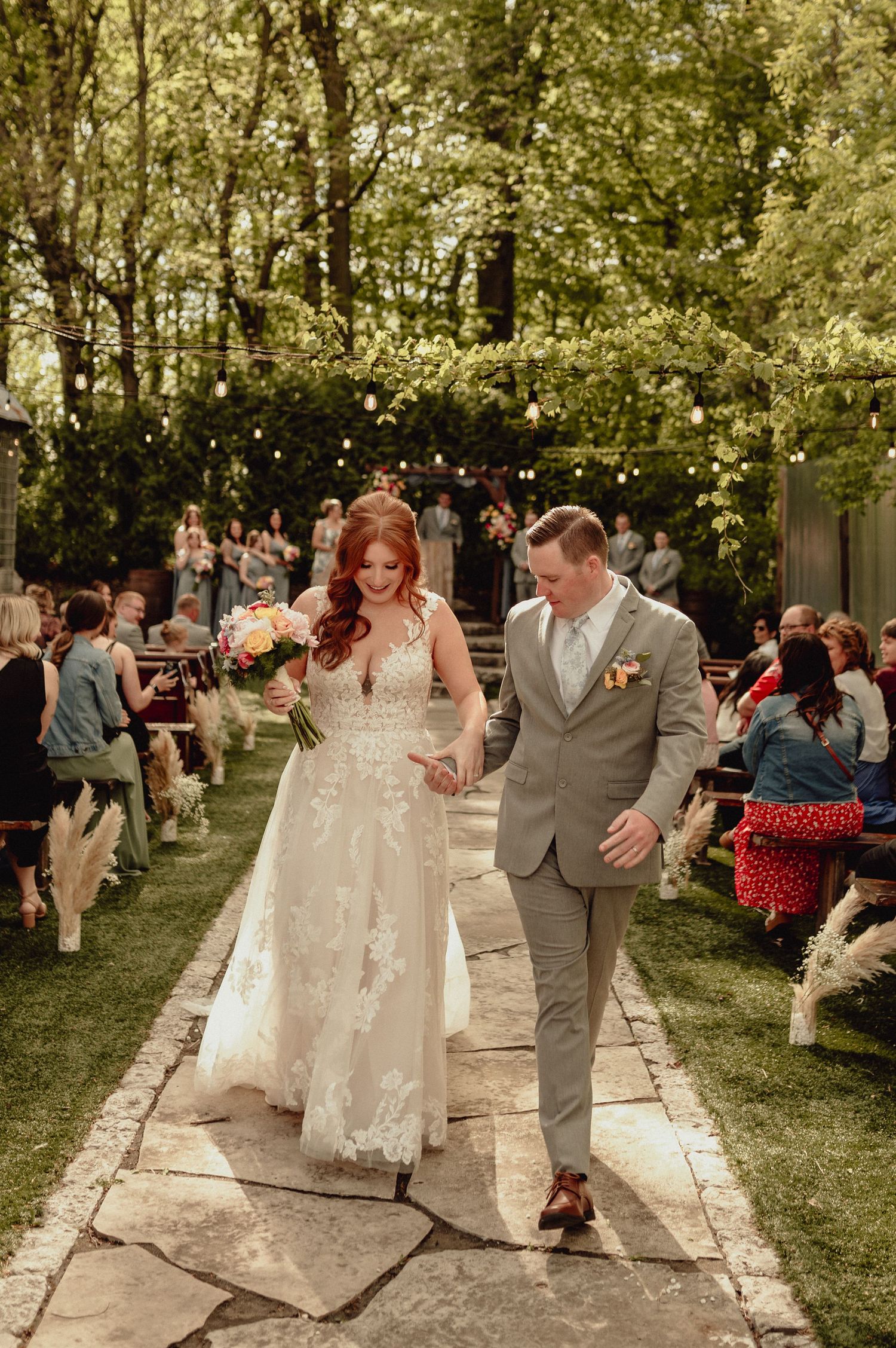 Joyful couple celebrates their outdoor garden wedding ceremony with guests gathered along a stone pathway.