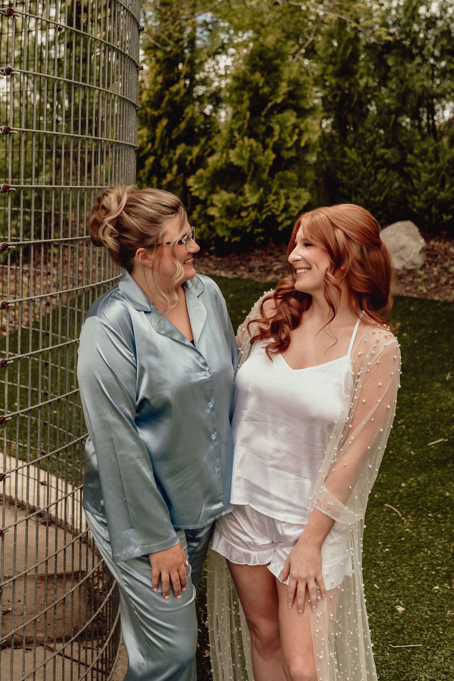 Two people in wedding attire share joyful moments together against a garden backdrop with ornate metal gates.