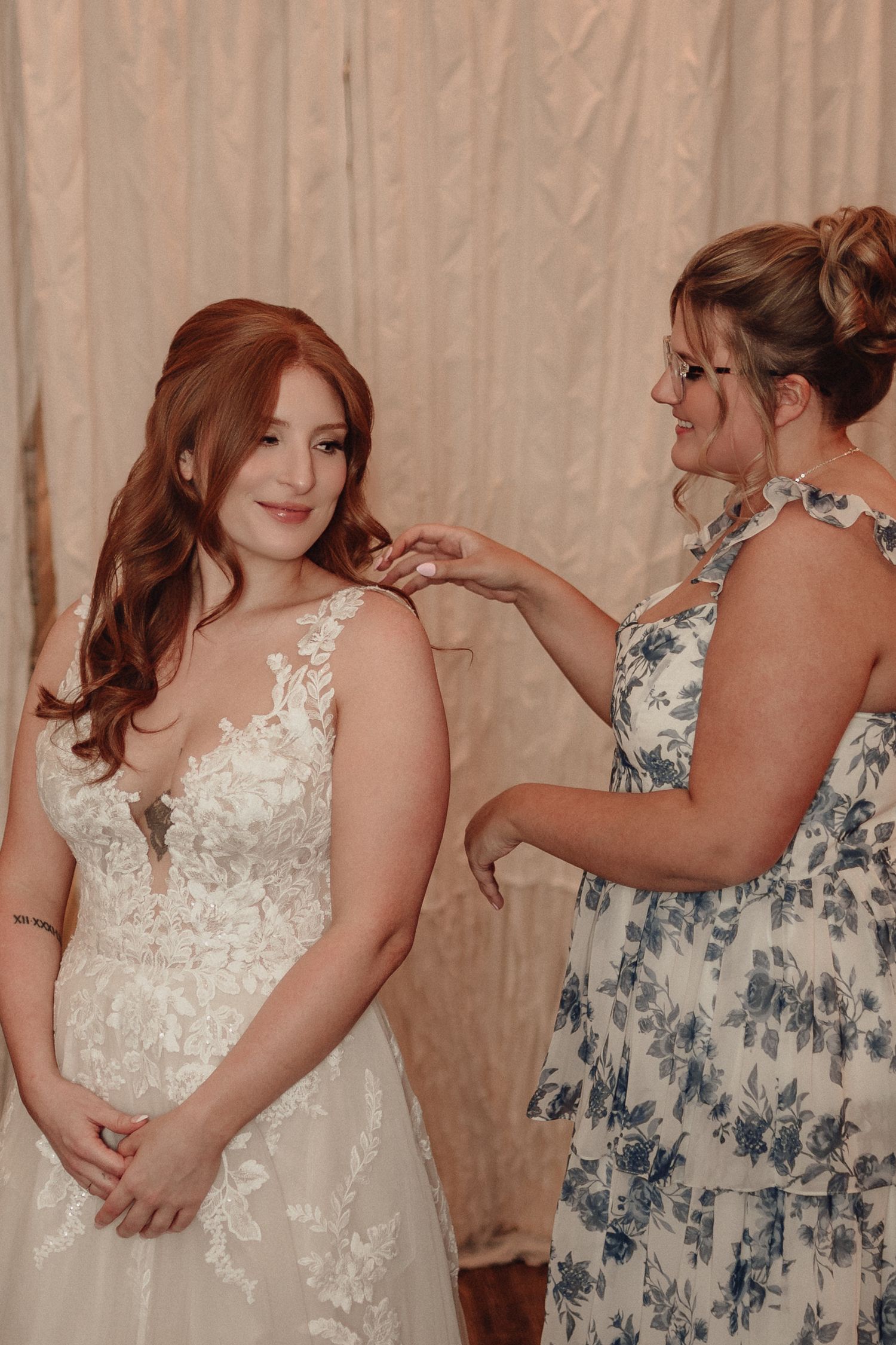 A tender moment as final adjustments are made to a beautiful lace wedding dress during bridal preparations.