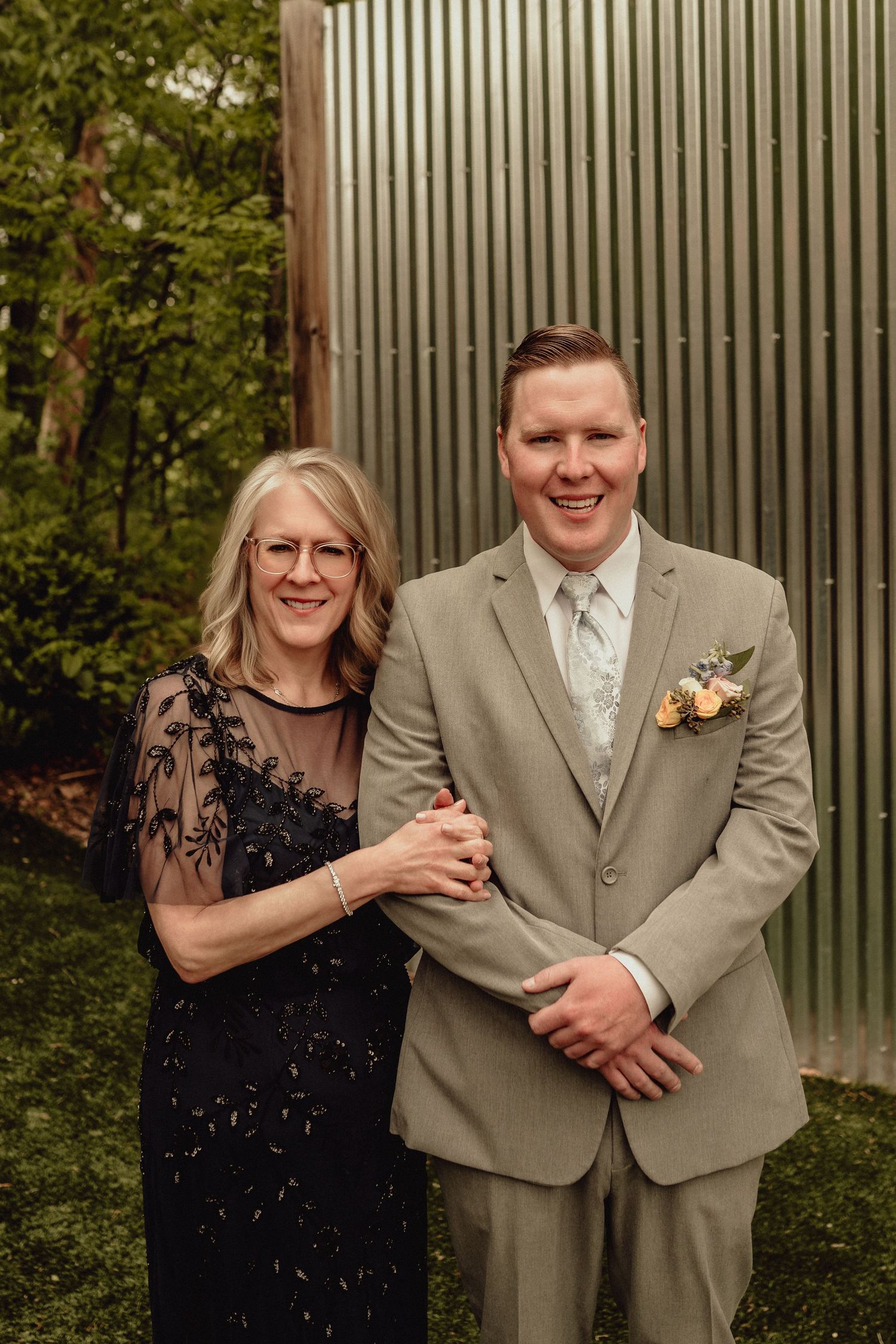 A couple in formal attire shares candid laughs and embraces during an outdoor photo session.