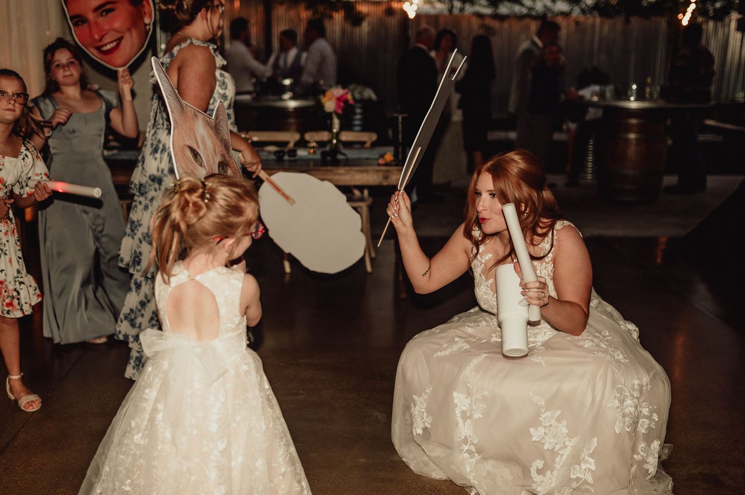 A young girl in a white dress dances with someone in a matching gown during a wedding reception celebration.