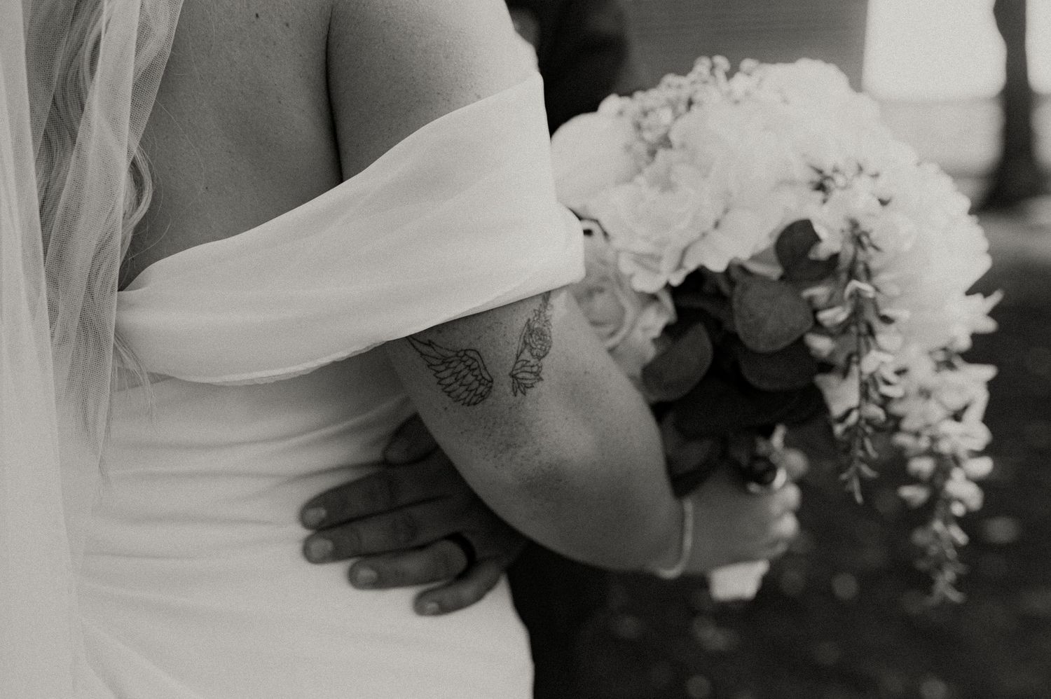 White bridal bouquet with delicate flowers and greenery against a dark background.