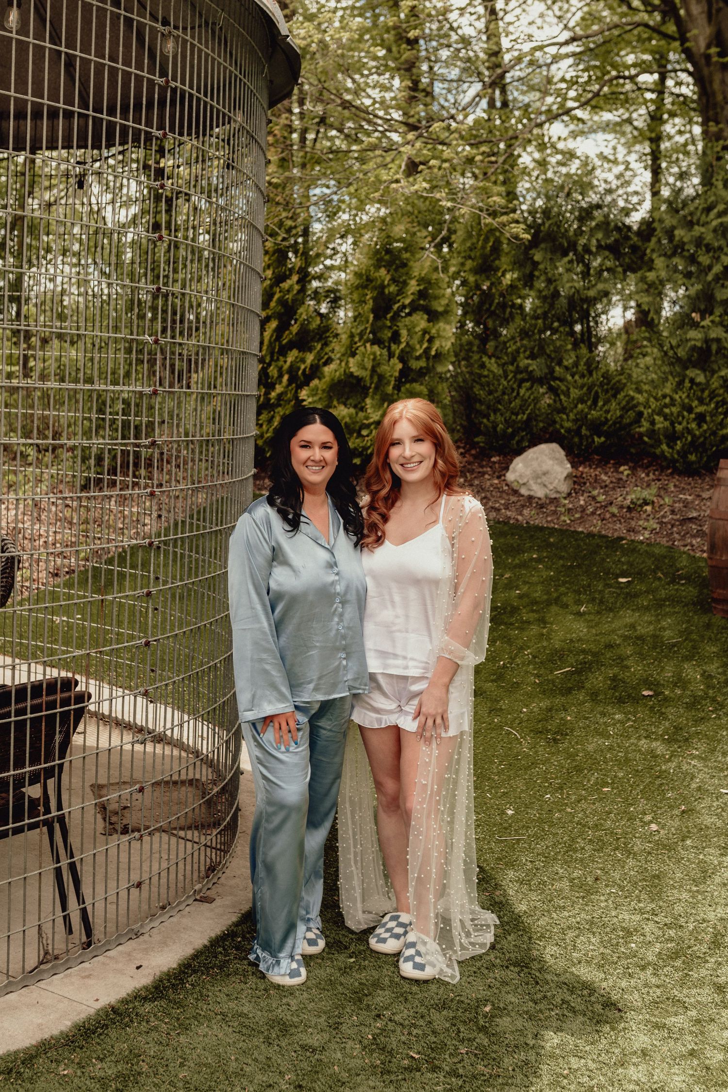 Two friends in matching pastel outfits pose together by a decorative metal gate in a garden setting.
