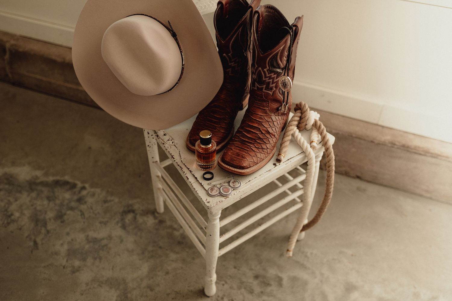 Rustic wedding decor featuring cowboy boots and hat on white furniture.