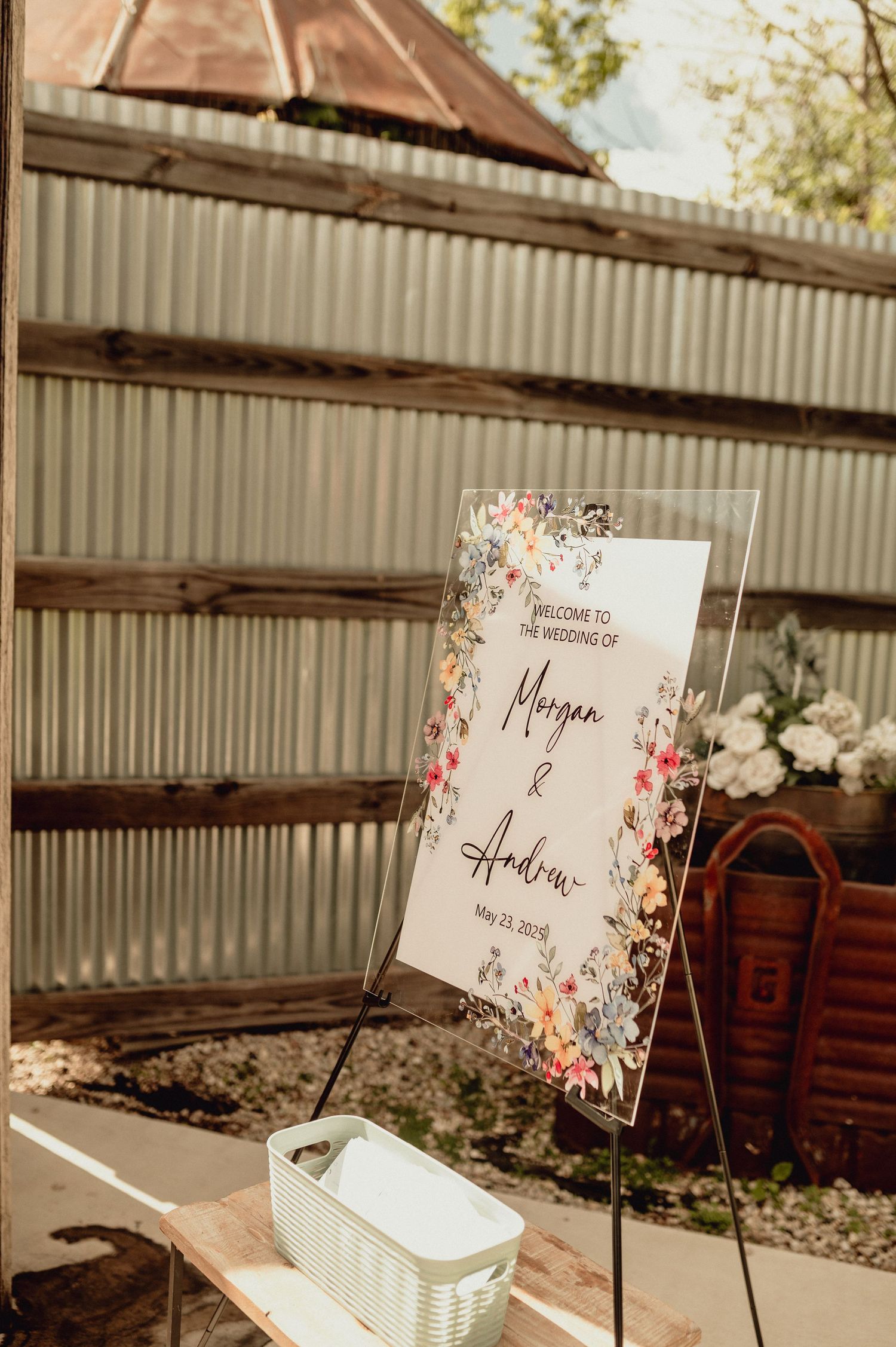 Wedding reception place cards with floral designs displayed on metal stands at a rustic venue.