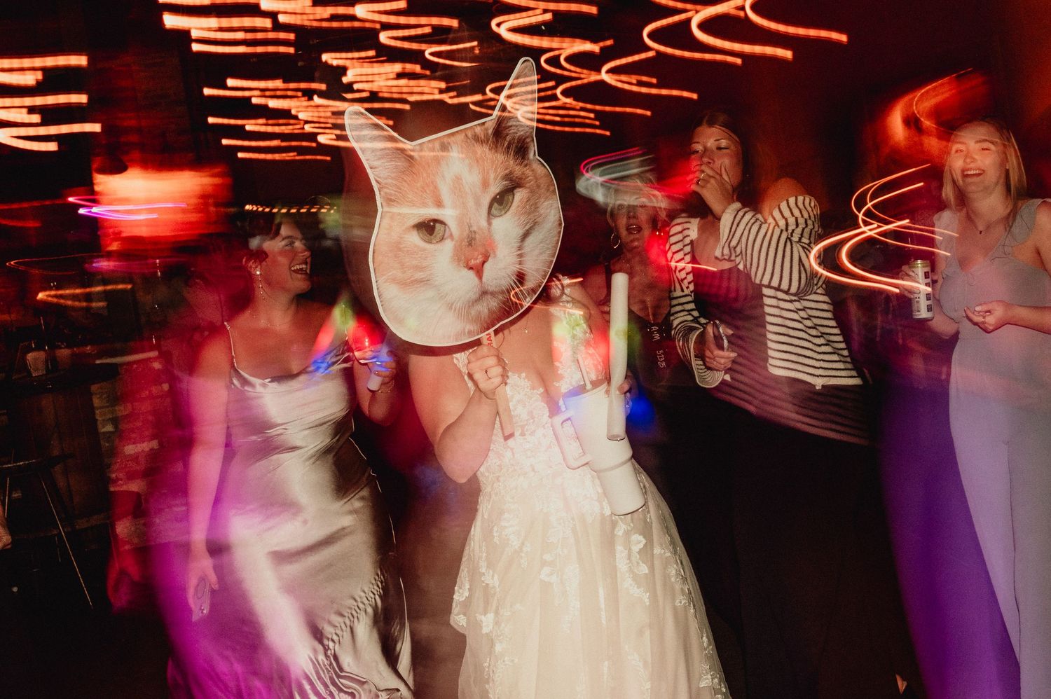People dancing at a wedding reception under orange and pink lighting effects with motion blur.