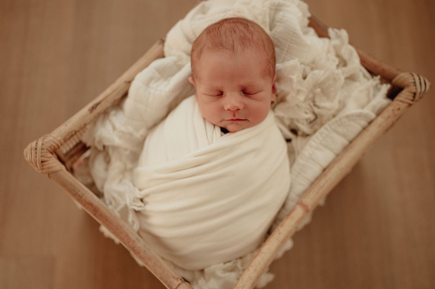 Newborn baby sleeping peacefully wrapped in white blanket.