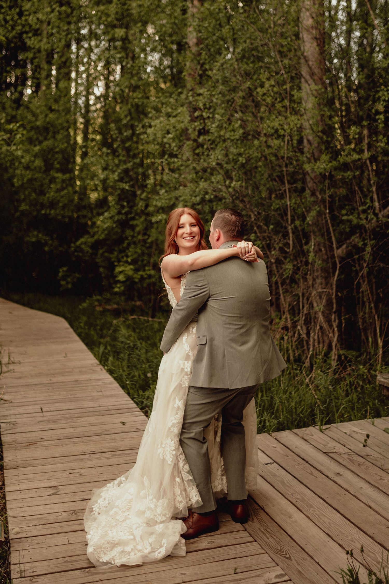 A couple embraces on a wooden boardwalk surrounded by lush green forest during their wedding photoshoot.