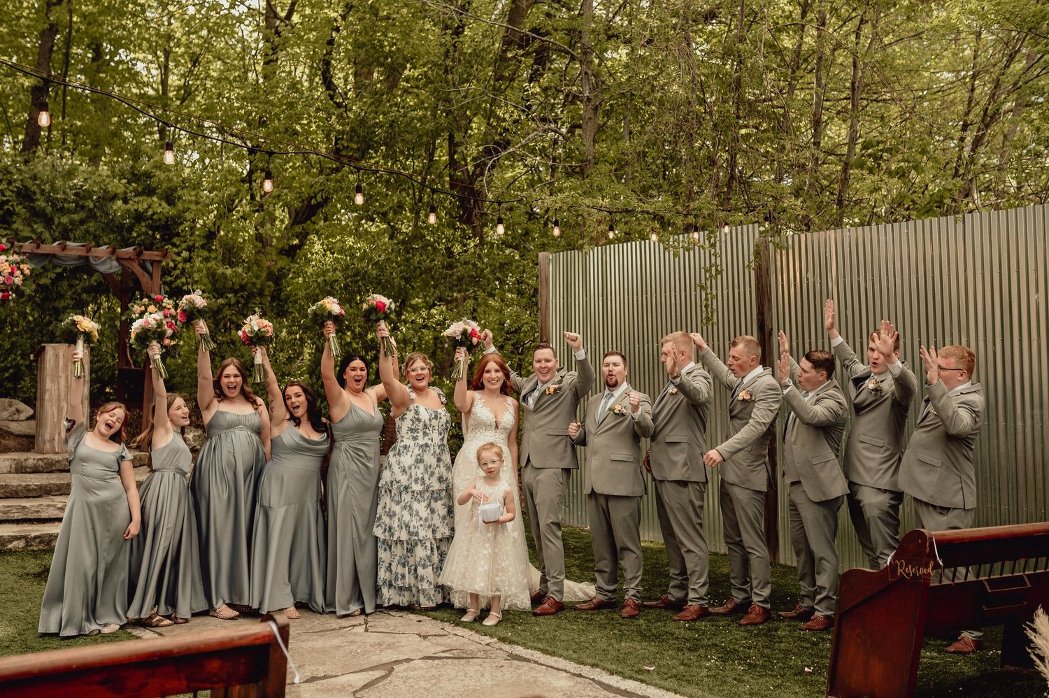 Wedding party poses together in a garden setting wearing gray and blush pink attire.