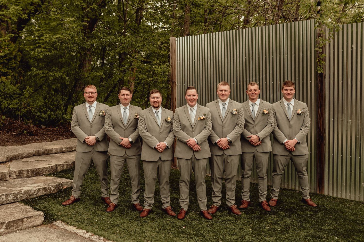 Wedding party members in gray suits and red socks pose playfully on stone steps in an outdoor garden setting.