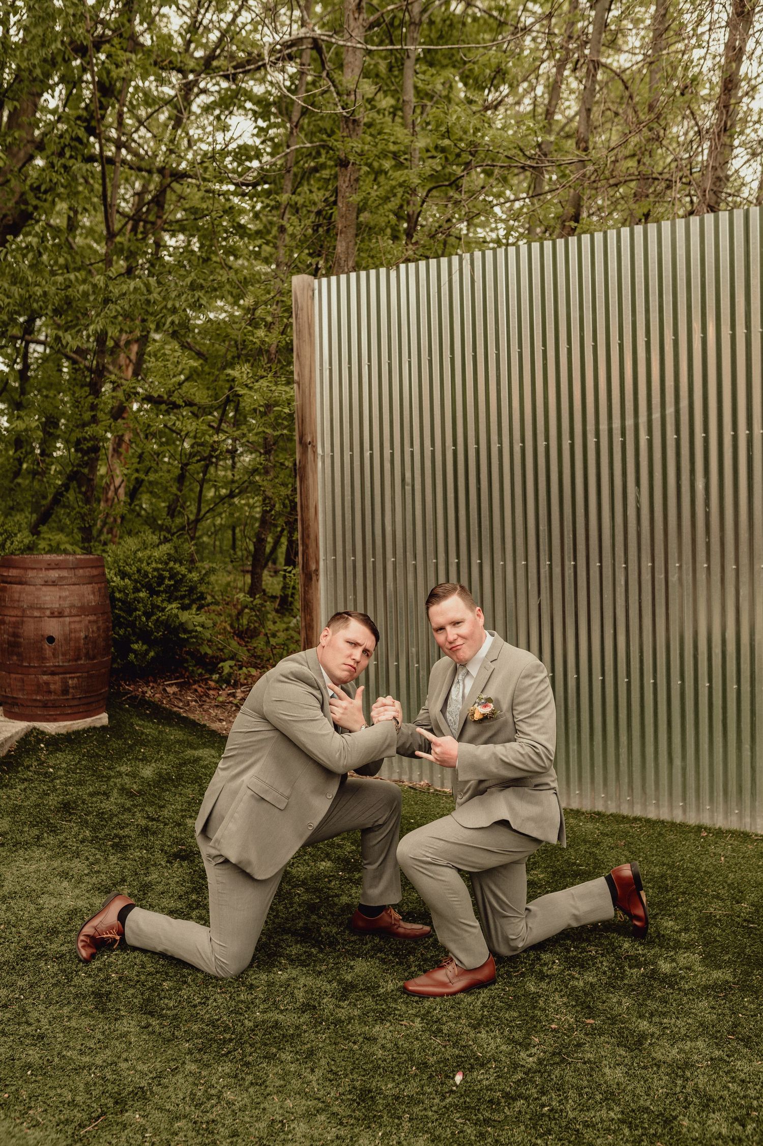 Two people in gray suits playfully wrestle on grass near a metal fence in a sequence of action shots.