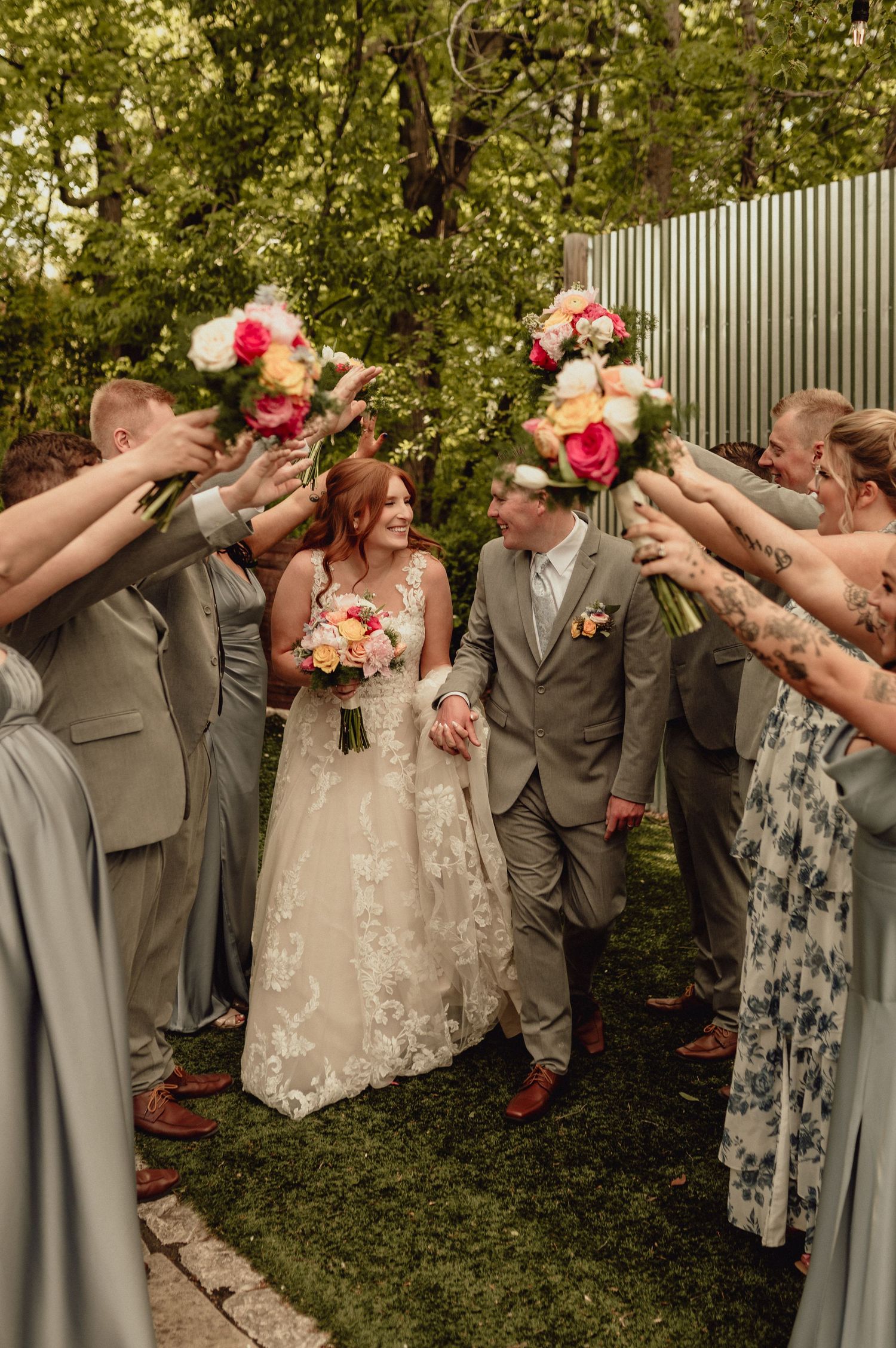 Wedding party members in gray suits and floral dresses raise their drinks in celebration during an outdoor photo session.